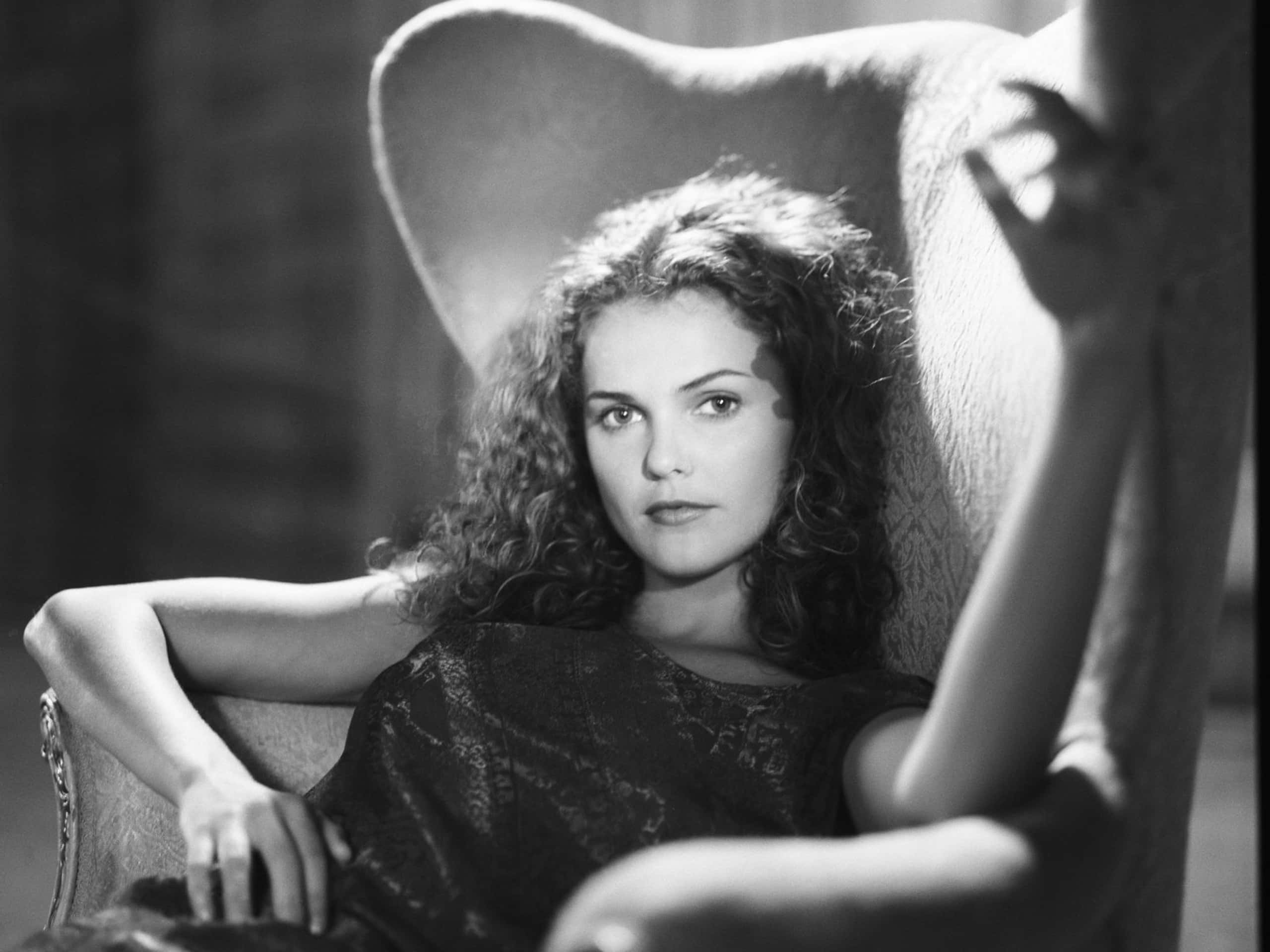 keri russell 桌布 壁紙 — 一位擁有捲髮的女性坐在高背椅上，在戲劇性的黑白肖像中直視鏡頭。