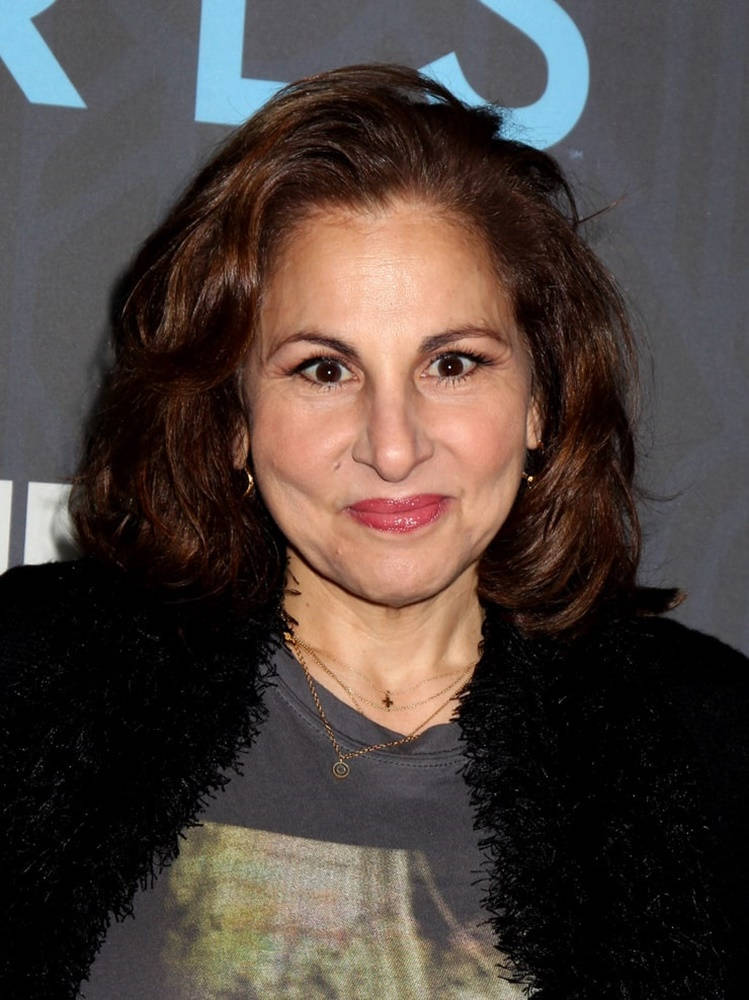 Celebrity 桌布 壁紙 — 一位擁有棕色波浪長髮的女性，穿著黑色絨毛外套搭配圖案T恤，對著鏡頭微笑。