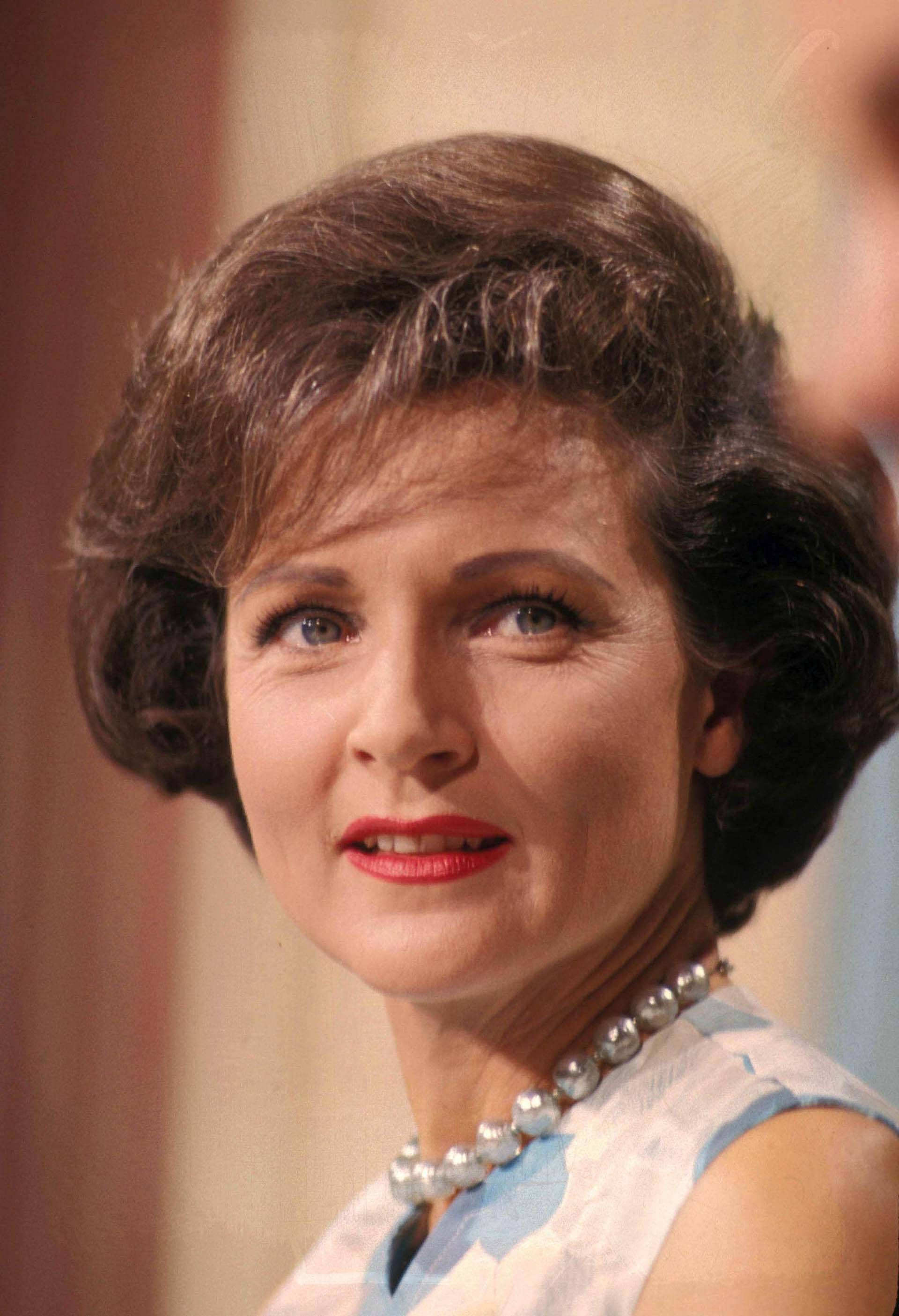 Betty White 桌布 壁紙 — 一位擁有棕色造型頭髮、紅唇和珍珠項鍊的女性，向上凝視，帶著溫柔微笑的復古肖像。