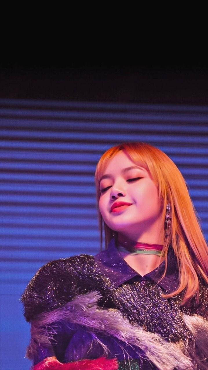 一位微笑的表演者，橙色頭髮，在藍色燈光舞台上穿著閃亮服裝。 — BLACKPINK Lisa GIF 壁紙