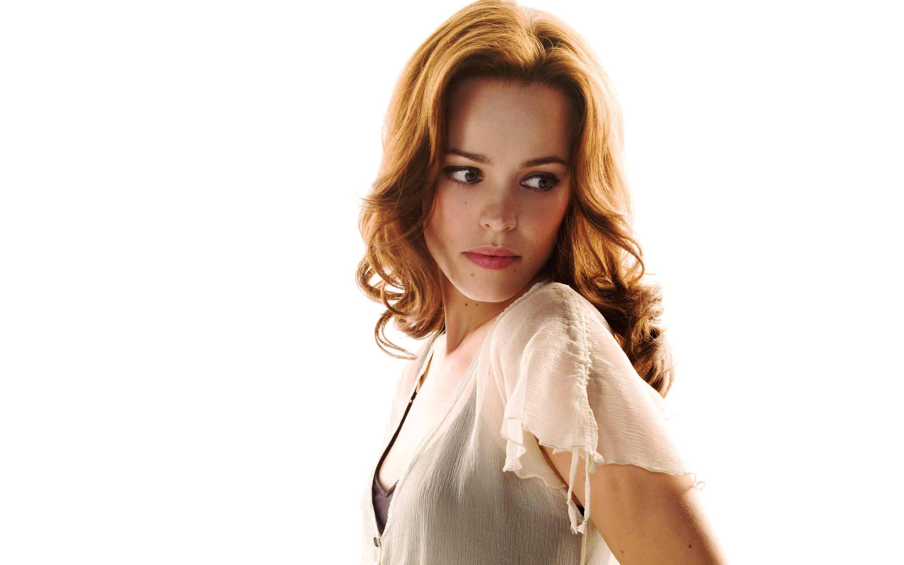 Rachel Mcadams 桌布 壁紙 — 一位擁有波浪形赤褐色頭髮和柔軟白色上衣的女性，在純白色背景上回頭望。