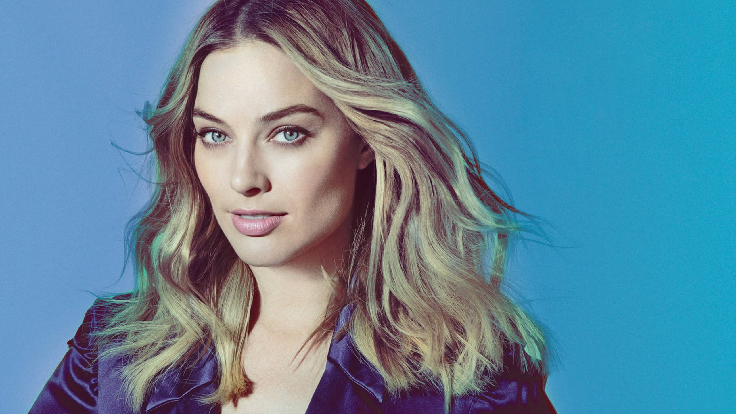 Margot Robbie 桌布 壁紙 — 一位擁有波浪形金髮和藍眼睛的女性，在純藍色背景下直視鏡頭。