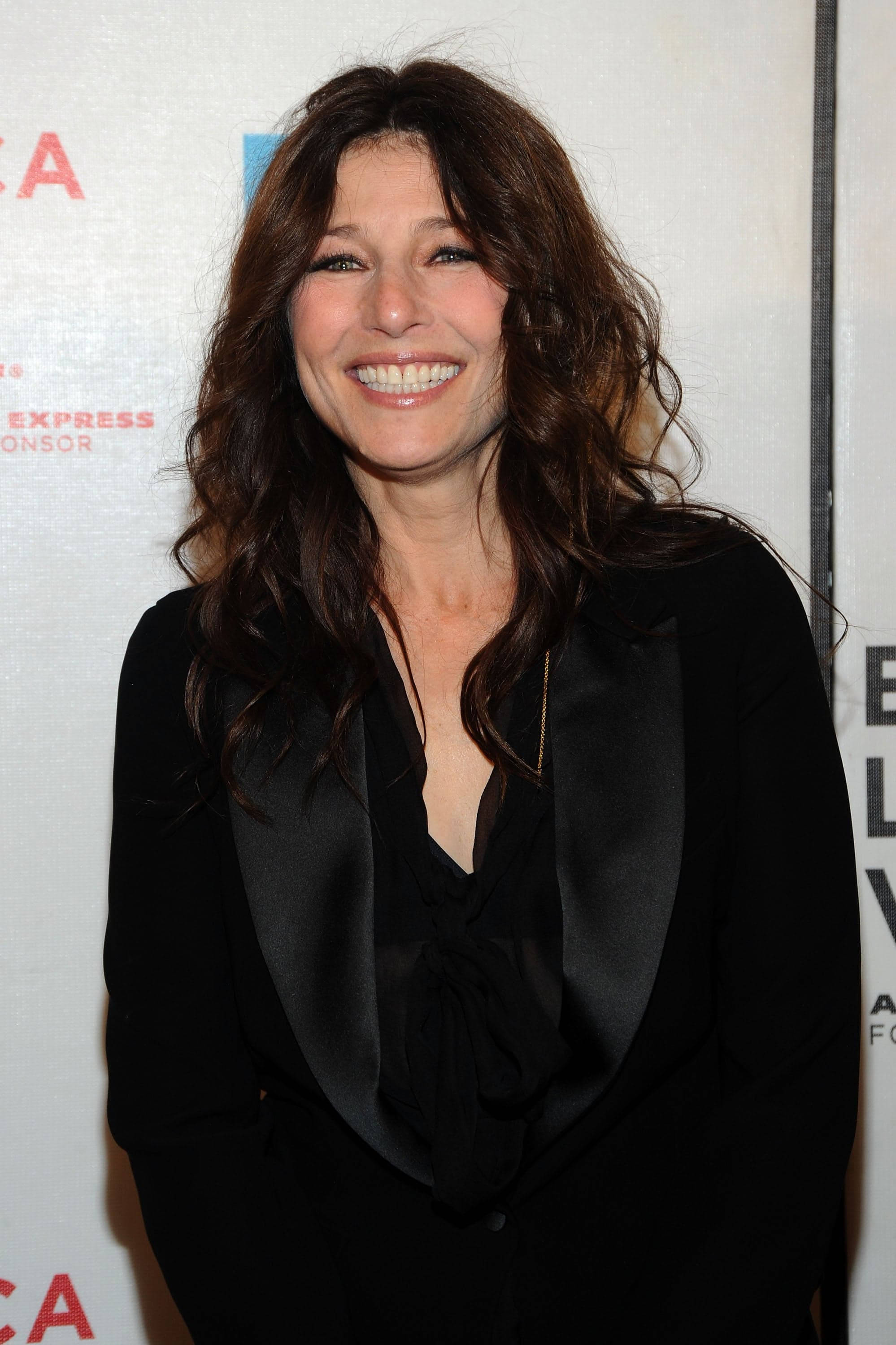 Celebrity 桌布 壁紙 — 一位擁有波浪棕色長髮的女性，在活動中穿著黑色緞面西裝外套，露出燦爛的笑容。