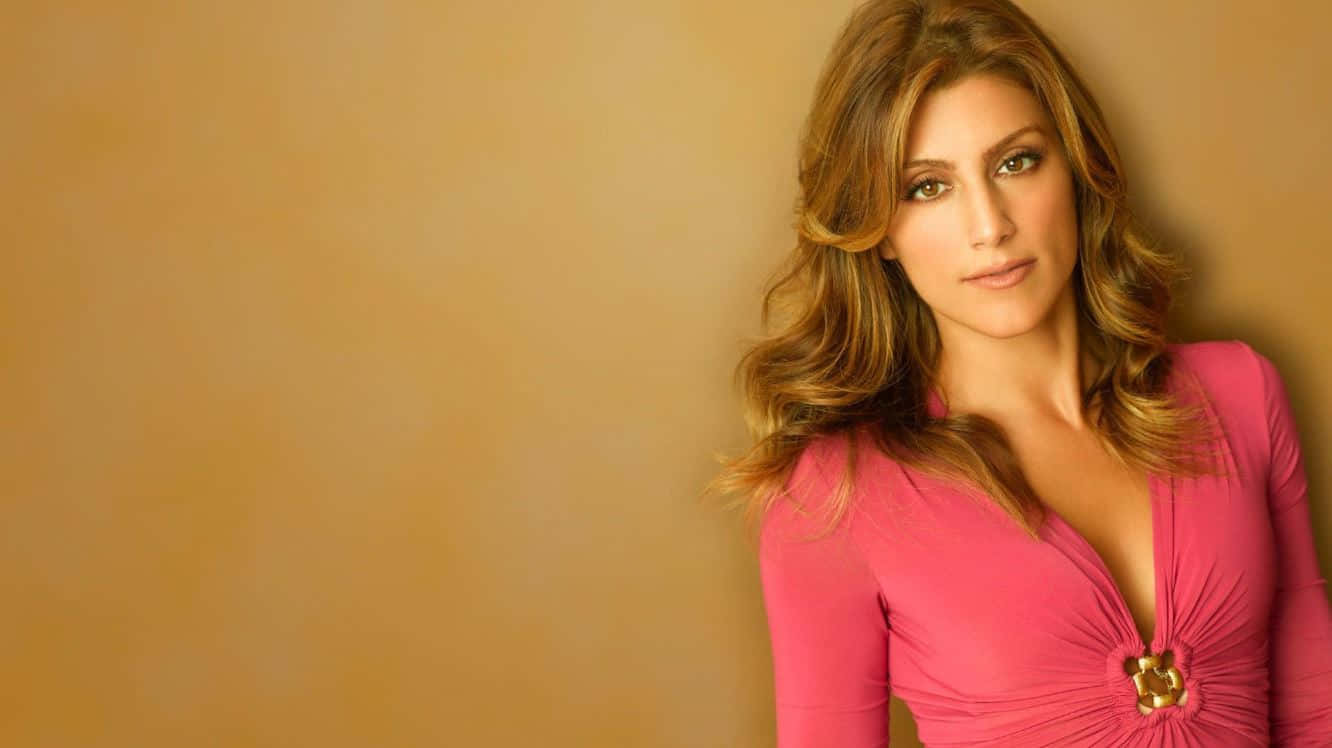 Jennifer Esposito 桌布 壁紙 — 一位擁有波浪棕色長髮的女性，身穿帶有金色紐扣的鮮豔粉紅色連衣裙，背景為溫暖的米色。