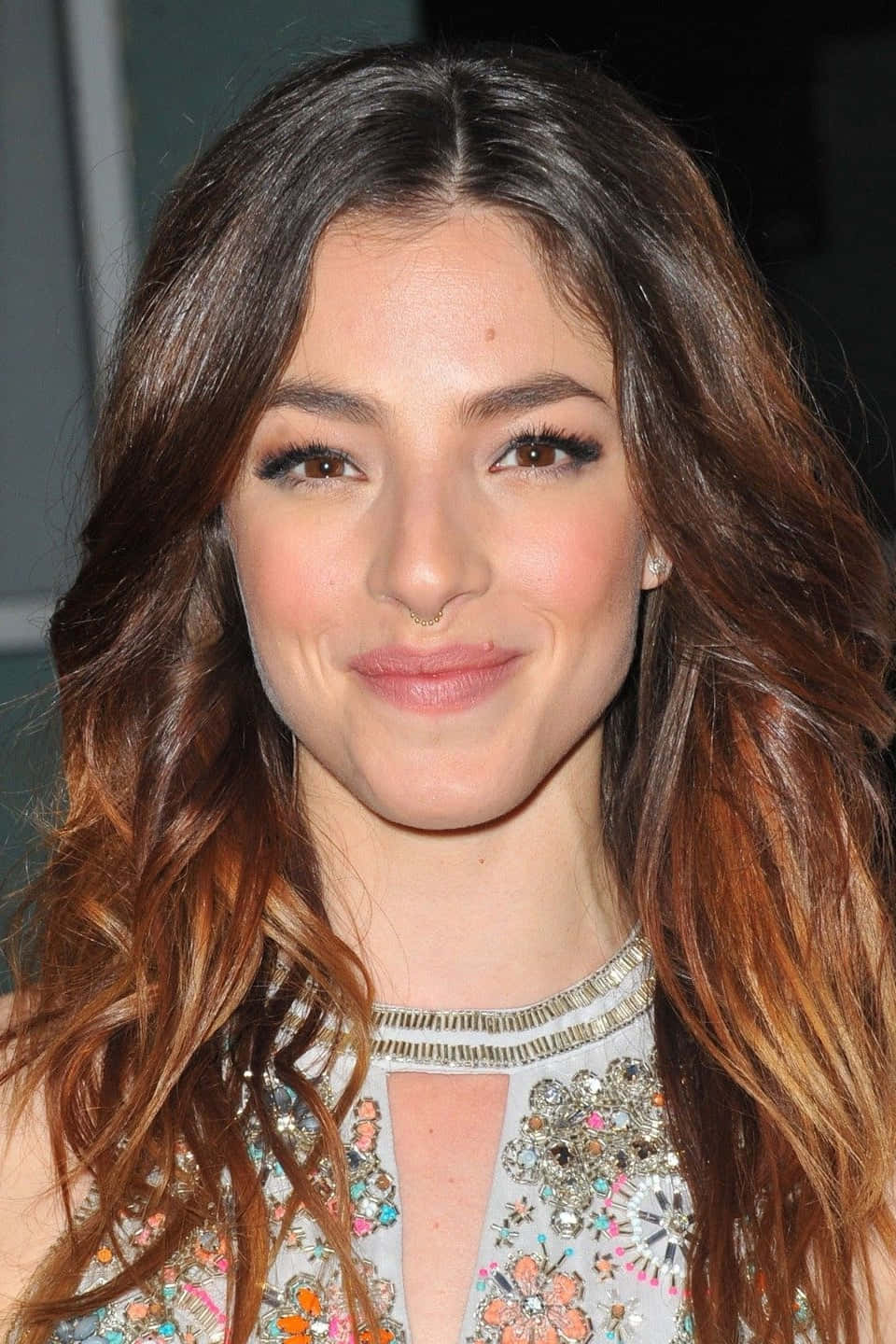 Olivia Thirlby 桌布 壁紙 — 一位擁有波浪棕色頭髮和含蓄微笑的女性，身穿華麗珠飾上衣的特寫肖像。