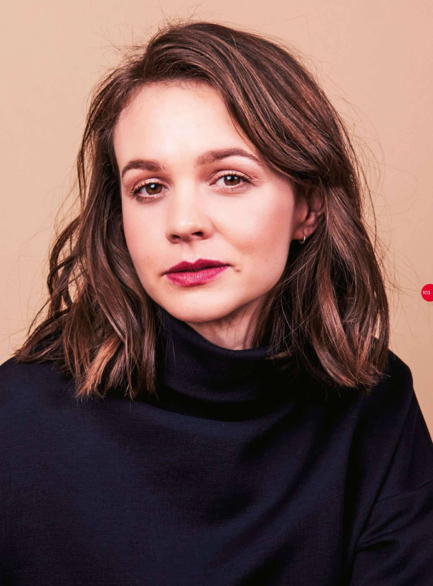 Carey Mulligan 桌布 壁紙 — 一位擁有波浪棕色頭髮和大膽紅唇的女性，在溫暖的米色背景下柔和地凝視。