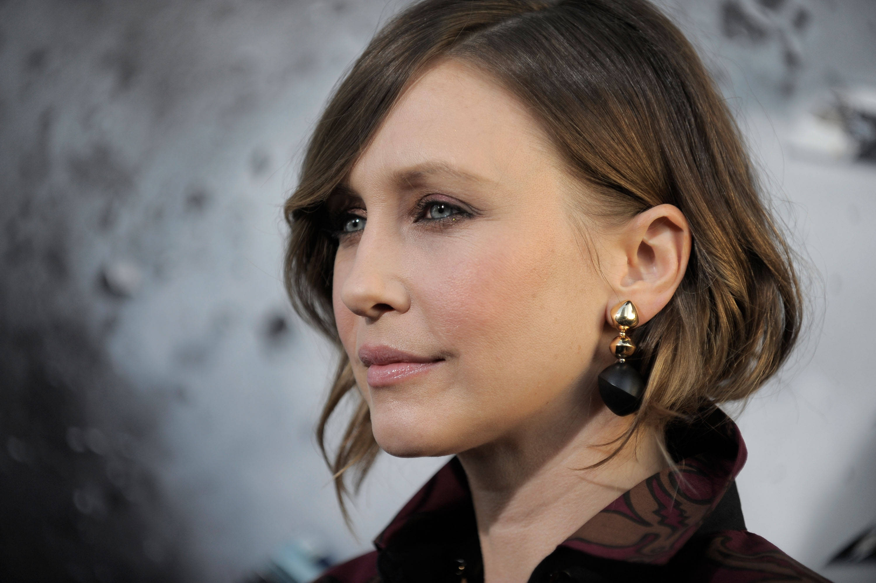 Celebrity 桌布 壁紙 — 一位擁有波浪棕色頭髮和引人注目的藍眼睛的女性的特寫肖像，戴著優雅的黑色和金色耳環。