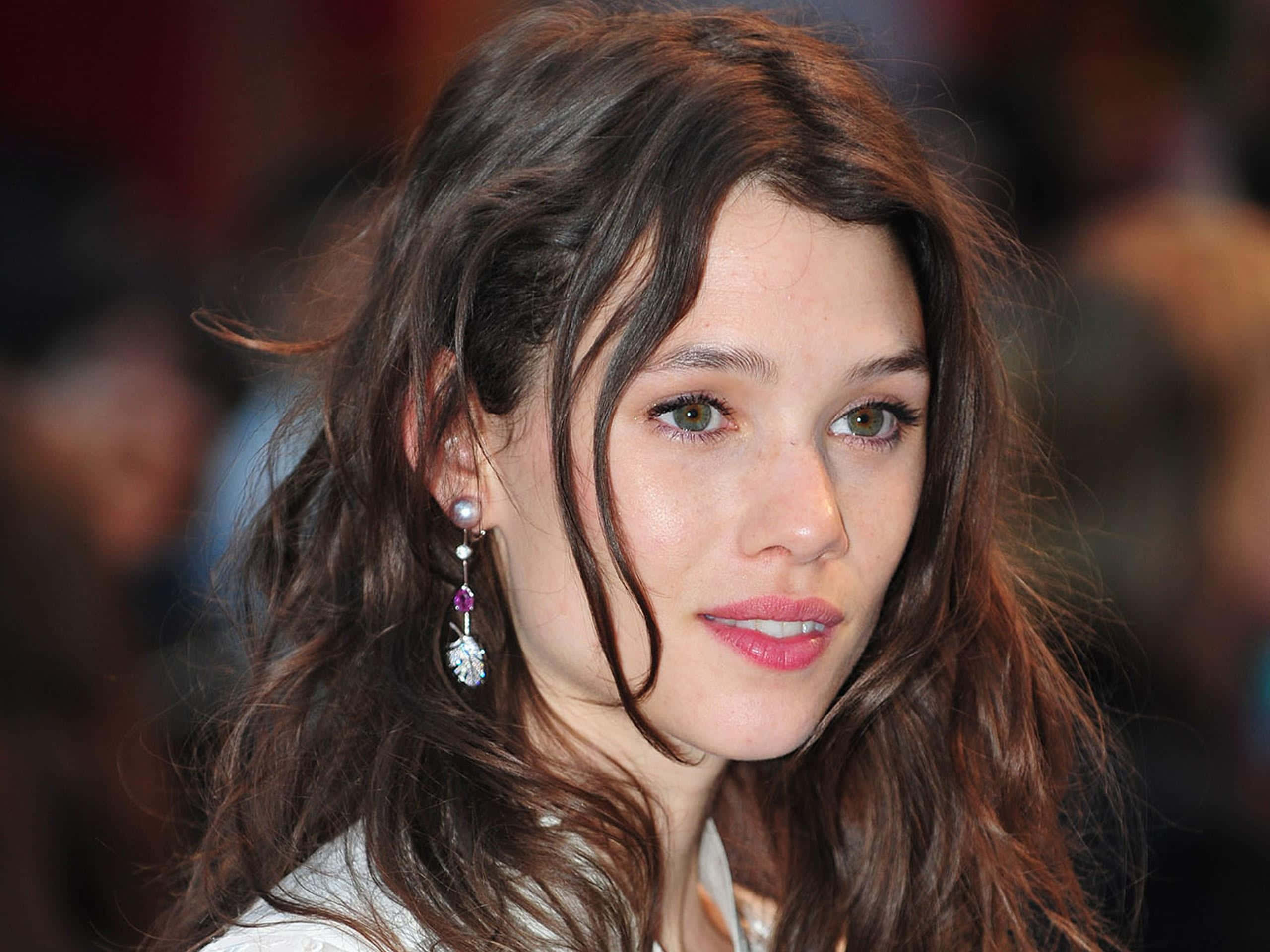 Astrid Berges Frisbey 桌布 壁紙 — 一位擁有波浪棕色頭髮和珍珠耳環的女性近距離肖像，對著鏡頭溫柔微笑。