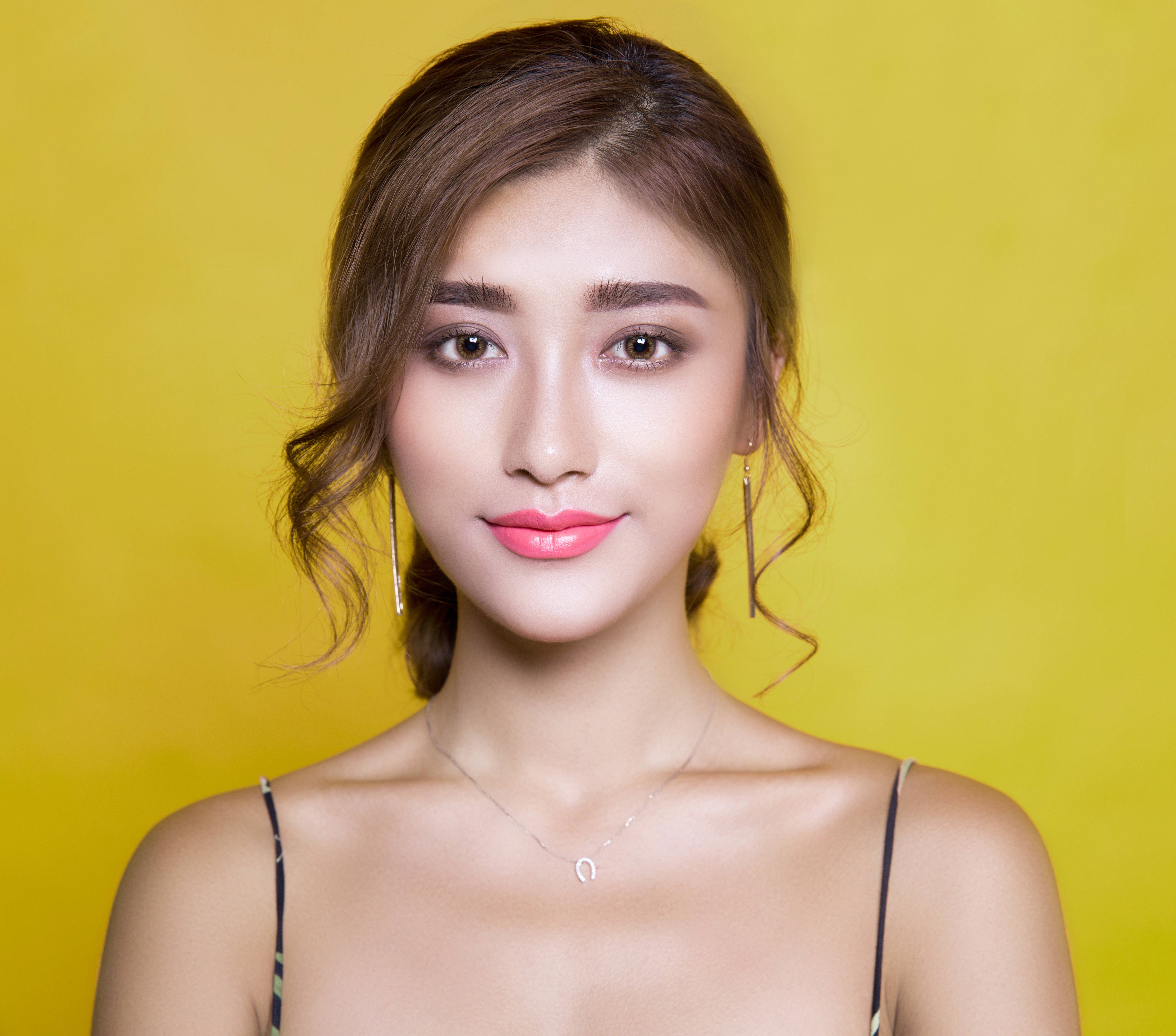 美女 桌布 壁紙 — 一位擁有波浪棕色頭髮和粉紅色唇膏的女性，在鮮黃色背景前溫柔微笑。