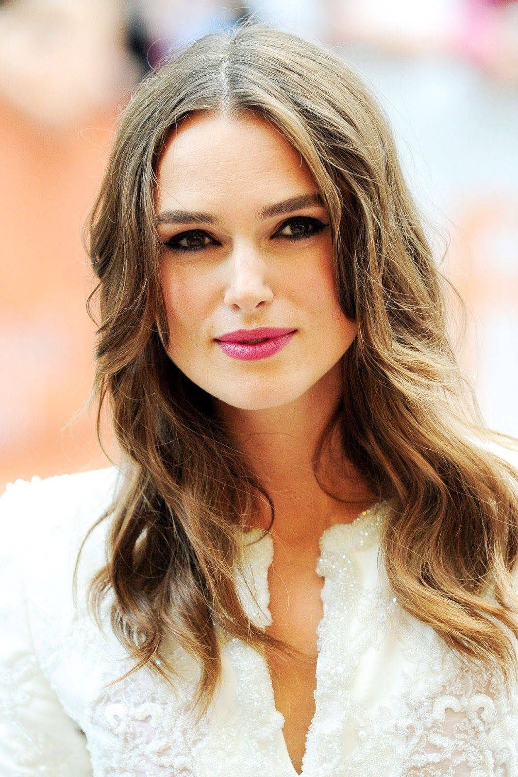 Keira Knightley 桌布 壁紙 — 一位擁有波浪棕色頭髮和粉紅色唇膏、穿著白色蕾絲上衣的女子的特寫肖像。