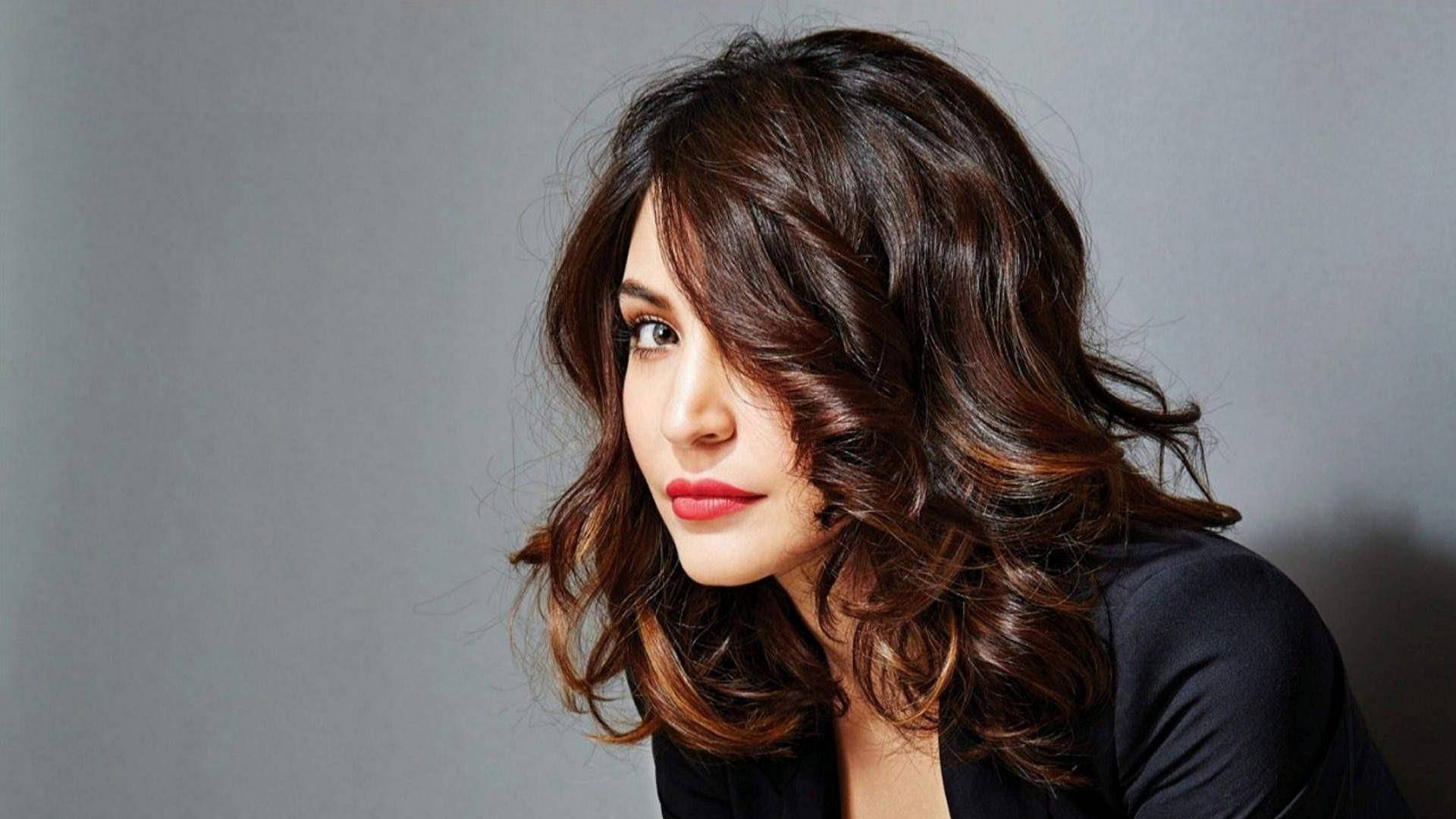 Anushka Sharma 桌布 壁紙 — 一位擁有波浪棕色頭髮和紅色唇膏的女性，在純灰色背景下若有所思地凝視著。