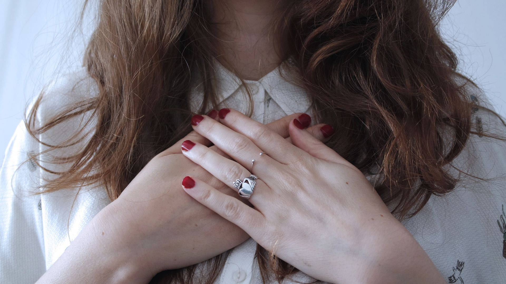 Ring 桌布 壁紙 — 一位擁有波浪棕色頭髮和紅色指甲的女性，戴著銀戒指，輕輕地將雙手交疊在胸前。
