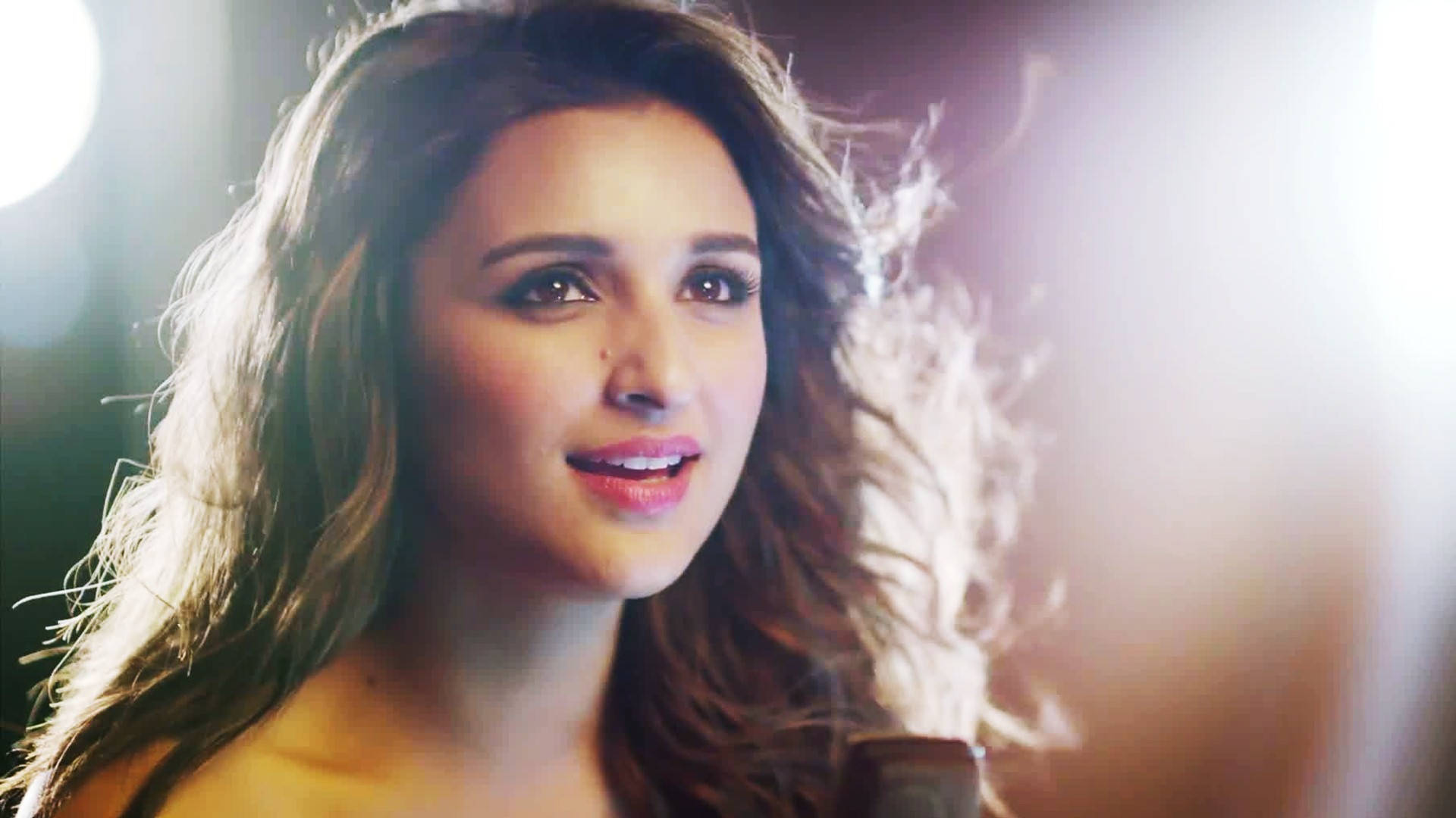 Parineeti 桌布 壁紙 — 一位擁有波浪棕色頭髮的女性，在溫暖的背光照射下，她的臉龐和髮絲被照亮，露出溫柔的微笑。