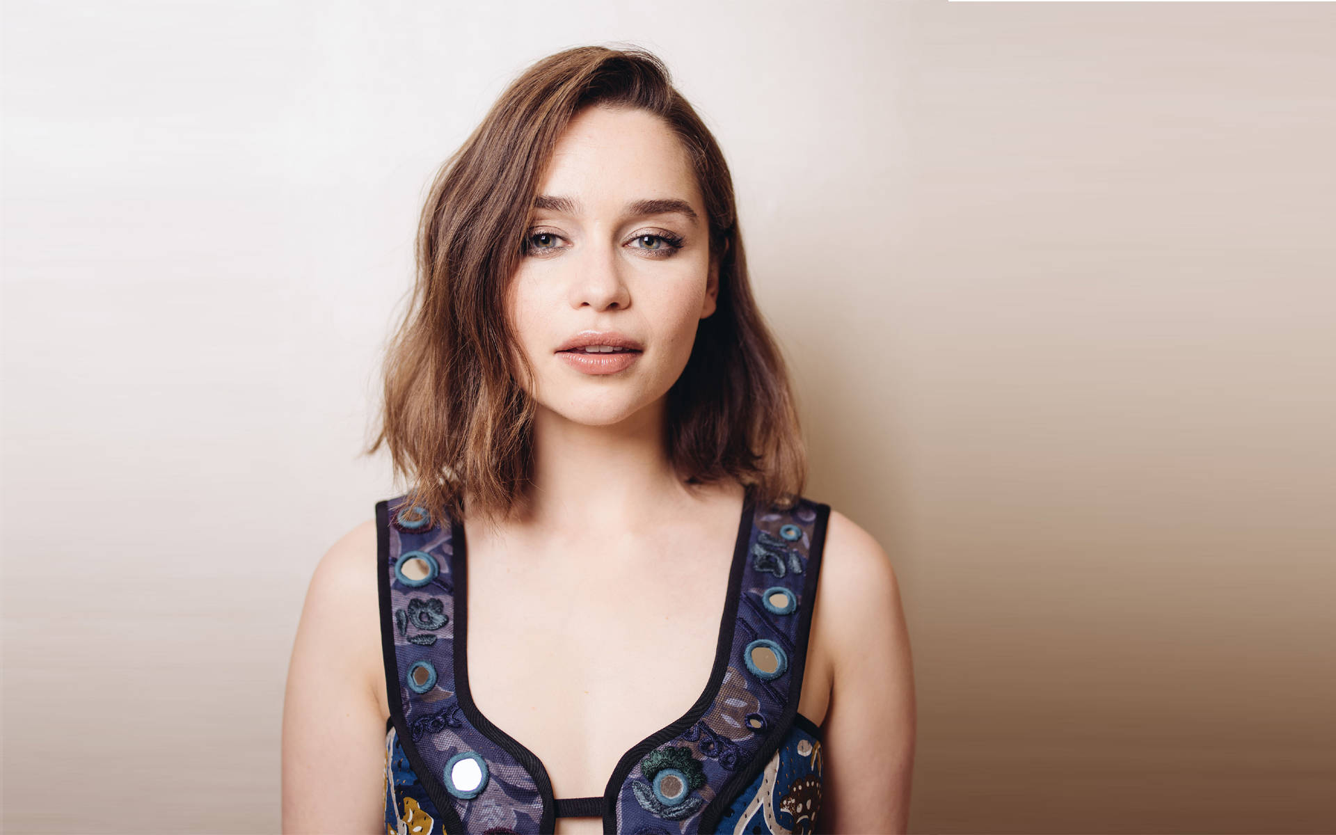 Emilia 桌布 壁紙 — 一位擁有波浪棕色頭髮的女性，穿著圖案藍色上衣，背景為柔和漸變色。