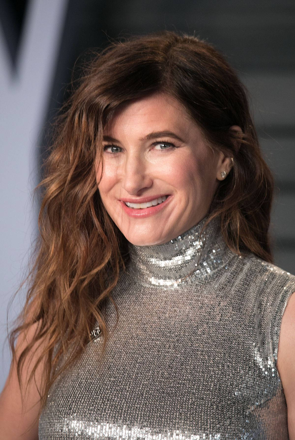 Celebrity 桌布 壁紙 — 一位擁有波浪棕色頭髮的女性，穿著閃亮的銀色亮片高領連衣裙，溫暖地微笑。