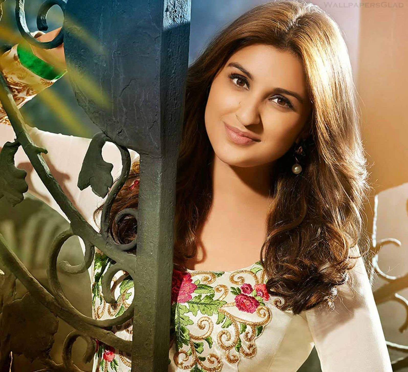 Parineeti 桌布 壁紙 — 一位擁有波浪棕色頭髮的女性，穿著花卉刺繡上衣，透過華麗的綠色金屬門窺視，溫柔地微笑。