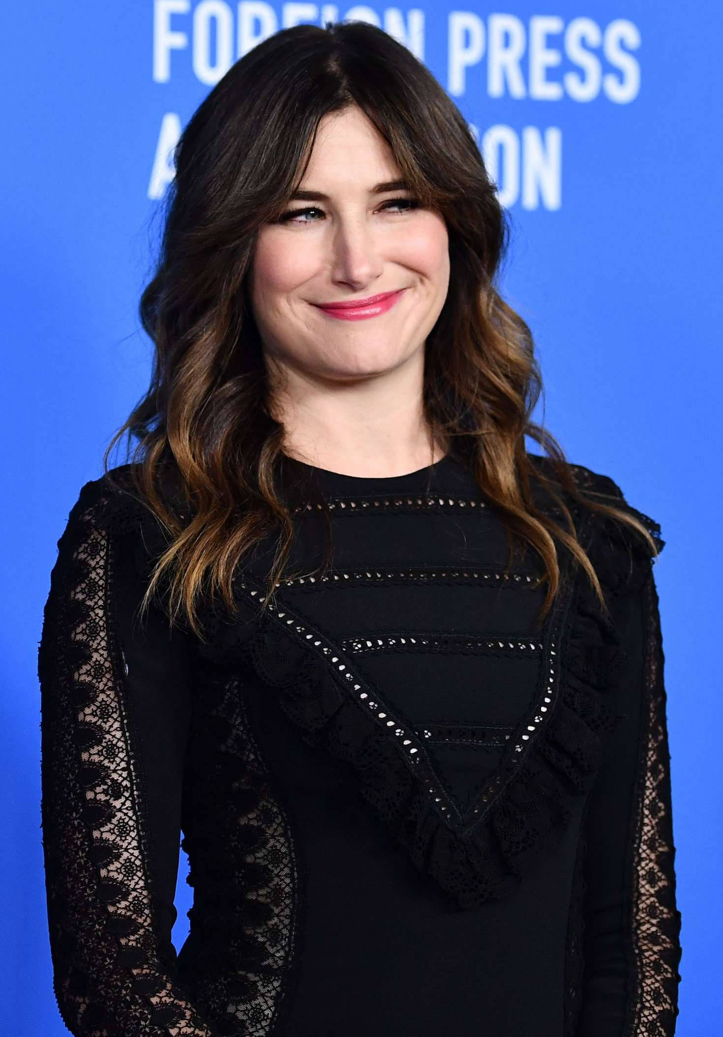 Celebrity 桌布 壁紙 — 一位擁有波浪棕色頭髮的女性，穿著黑色蕾絲連衣裙，在藍色活動背景前溫暖地微笑。