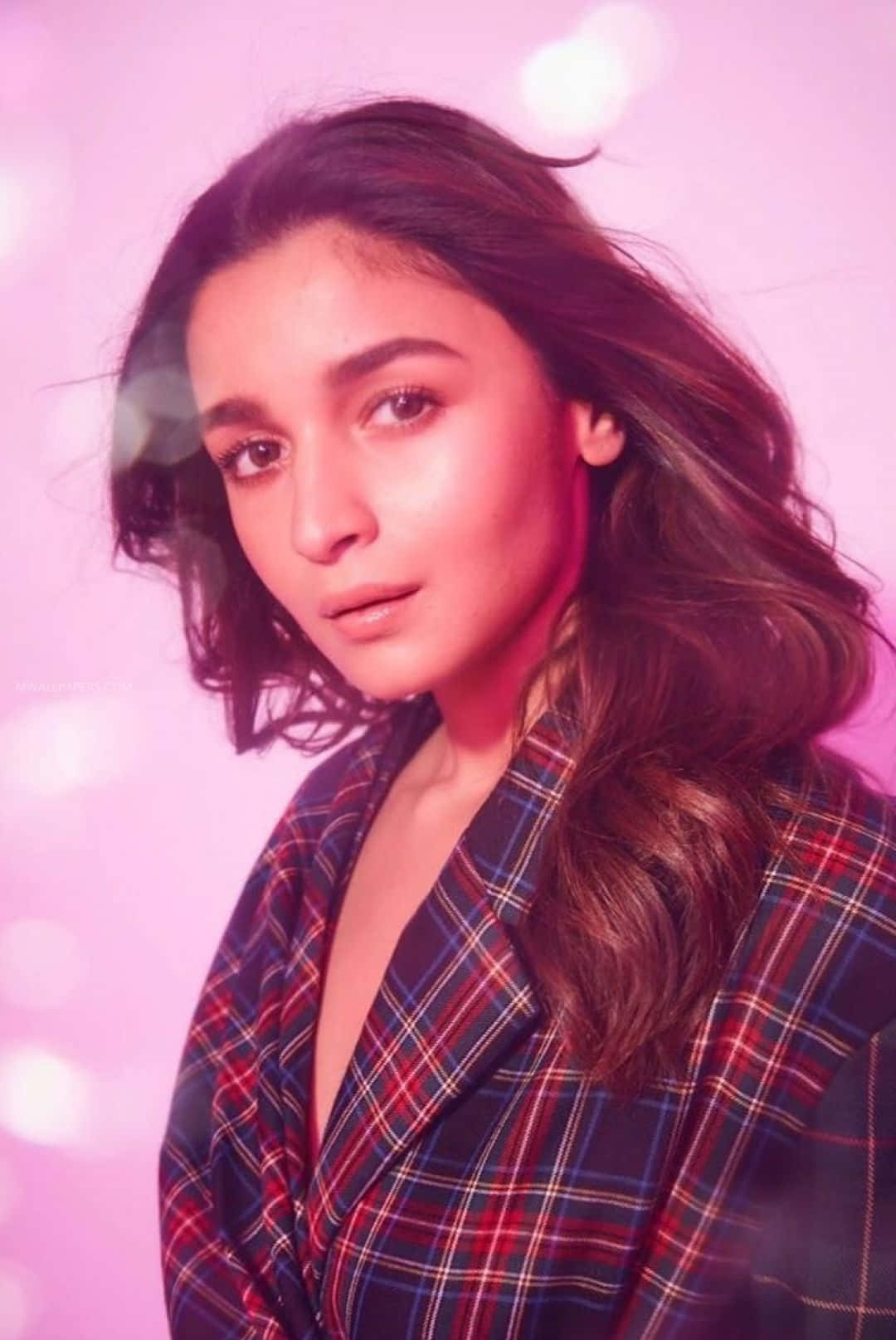 Alia Bhatt 桌布 壁紙 — 一位擁有波浪棕色頭髮的女性，穿著格紋西裝外套，背景是柔和的粉紅色散景。