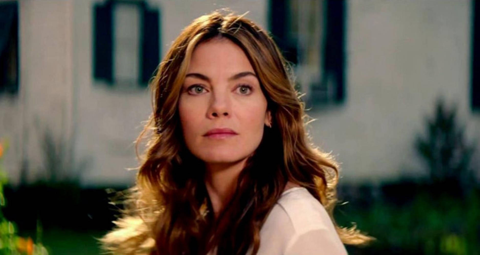 Michelle Monaghan 桌布 壁紙 — 一位擁有波浪棕色頭髮的女性在柔和自然光線下，以模糊的房子背景為襯托，直視鏡頭。