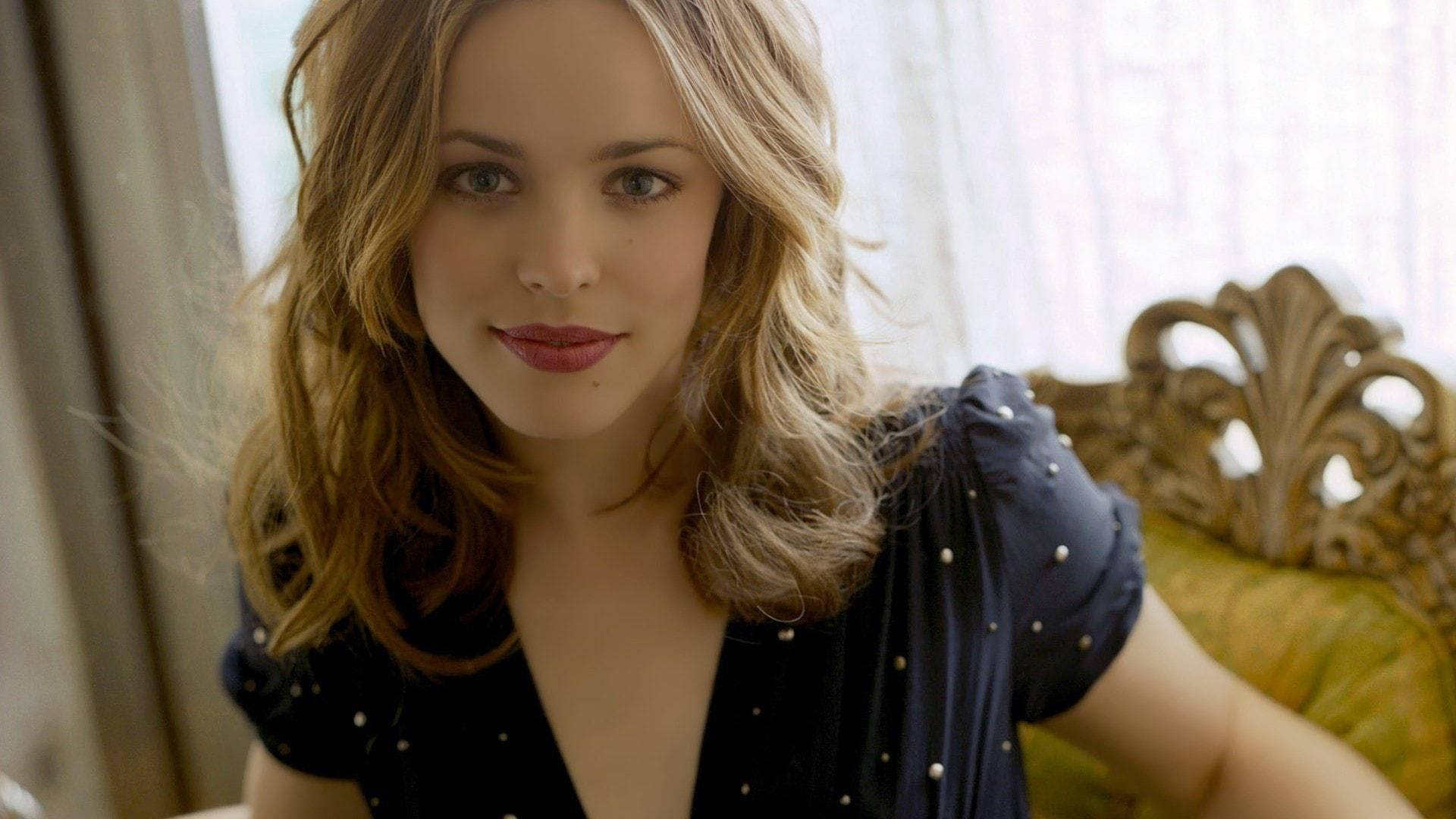 Rachel Mcadams 桌布 壁紙 — 一位擁有波浪金髮和紅唇的女性坐在裝飾華麗的金色椅子上，房間光線柔和。