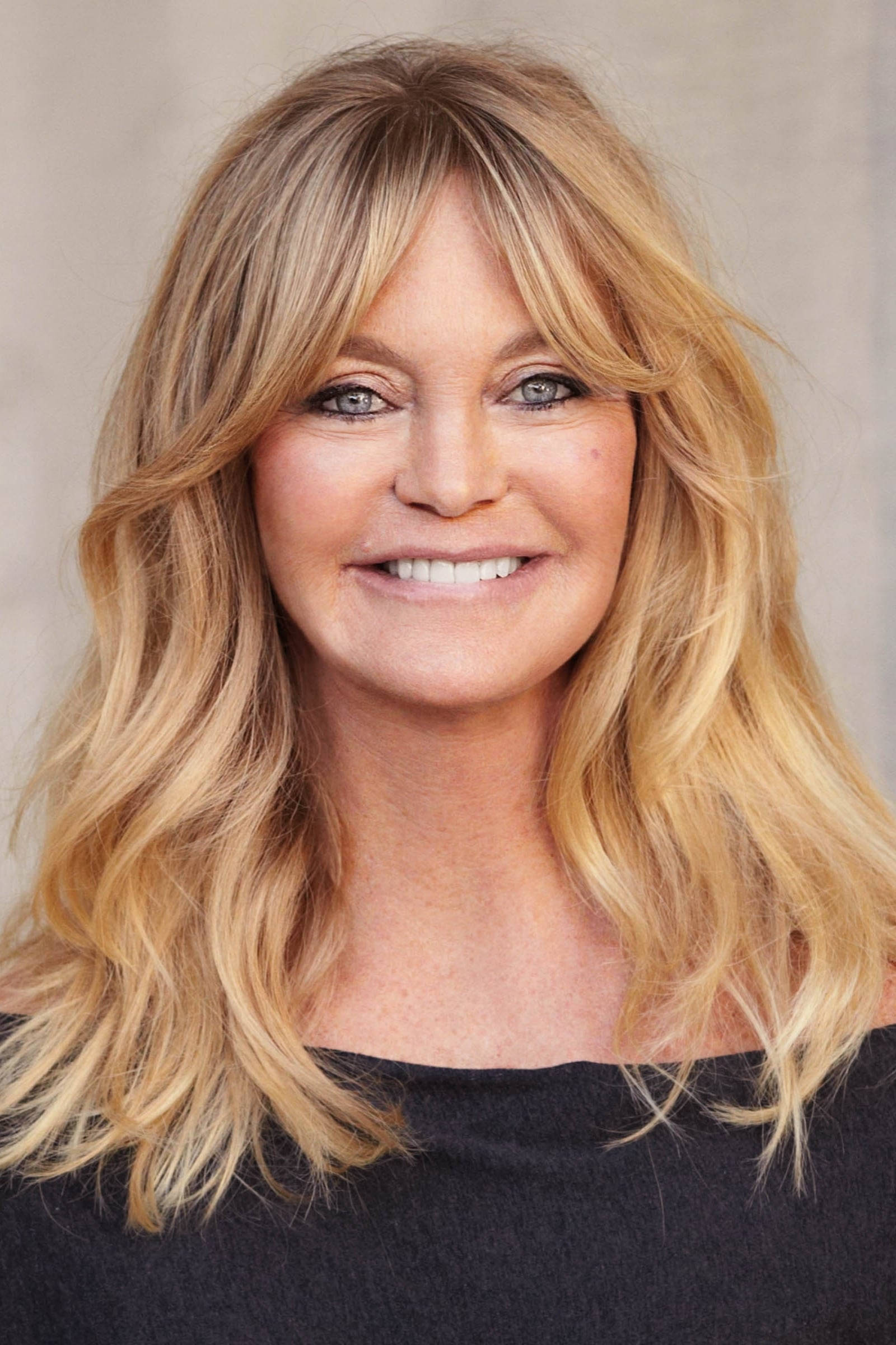 Celebrity 桌布 壁紙 — 一位擁有波浪金髮和藍眼睛的女性，在中性米色背景前溫暖地微笑。