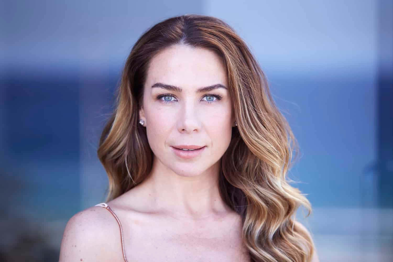 Kate Ritchie 桌布 壁紙 — 一位擁有波浪金髮和藍眼睛的女性，在模糊的藍色背景下溫柔地凝視著相機。