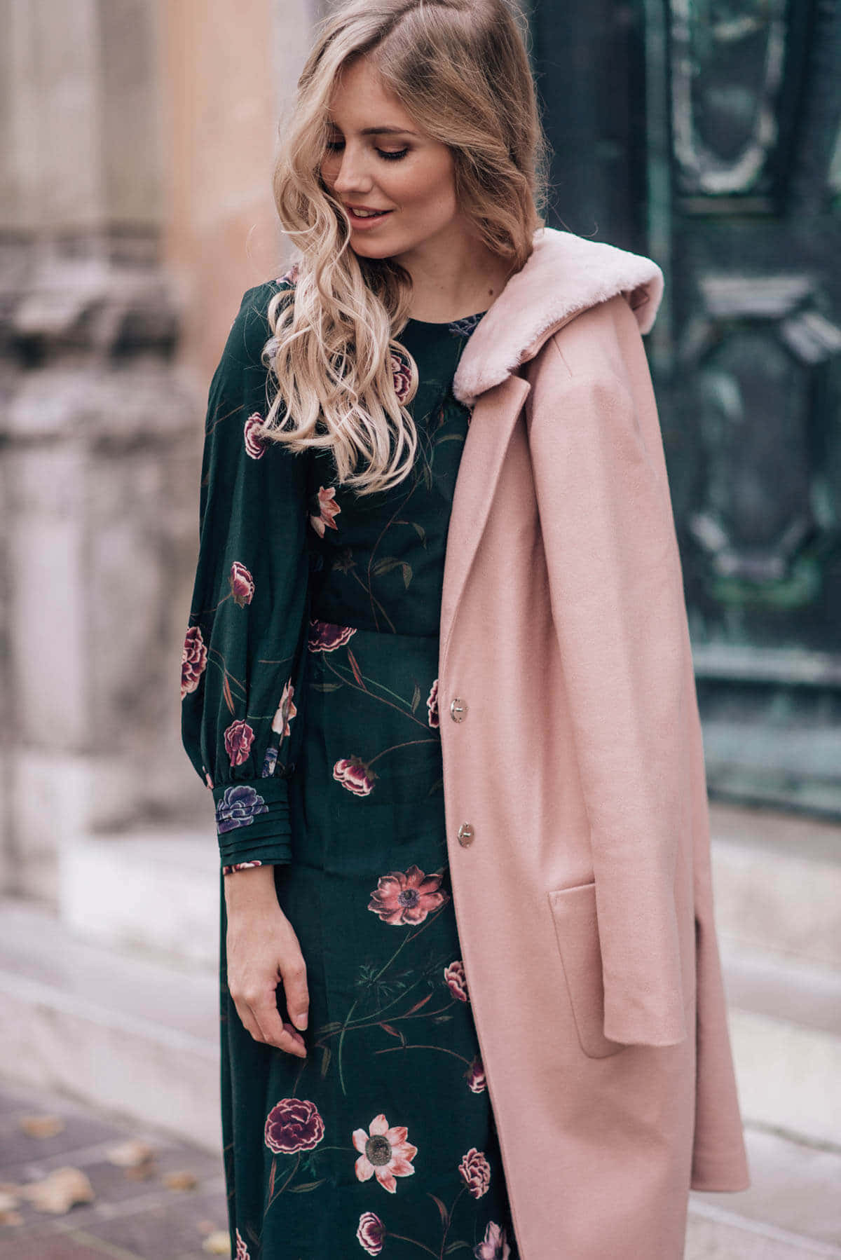 Pink Coat 桌布 壁紙 — 一位擁有波浪金髮的女性，在城市人行道上穿著花卉綠色連衣裙和帶毛領的粉色外套。