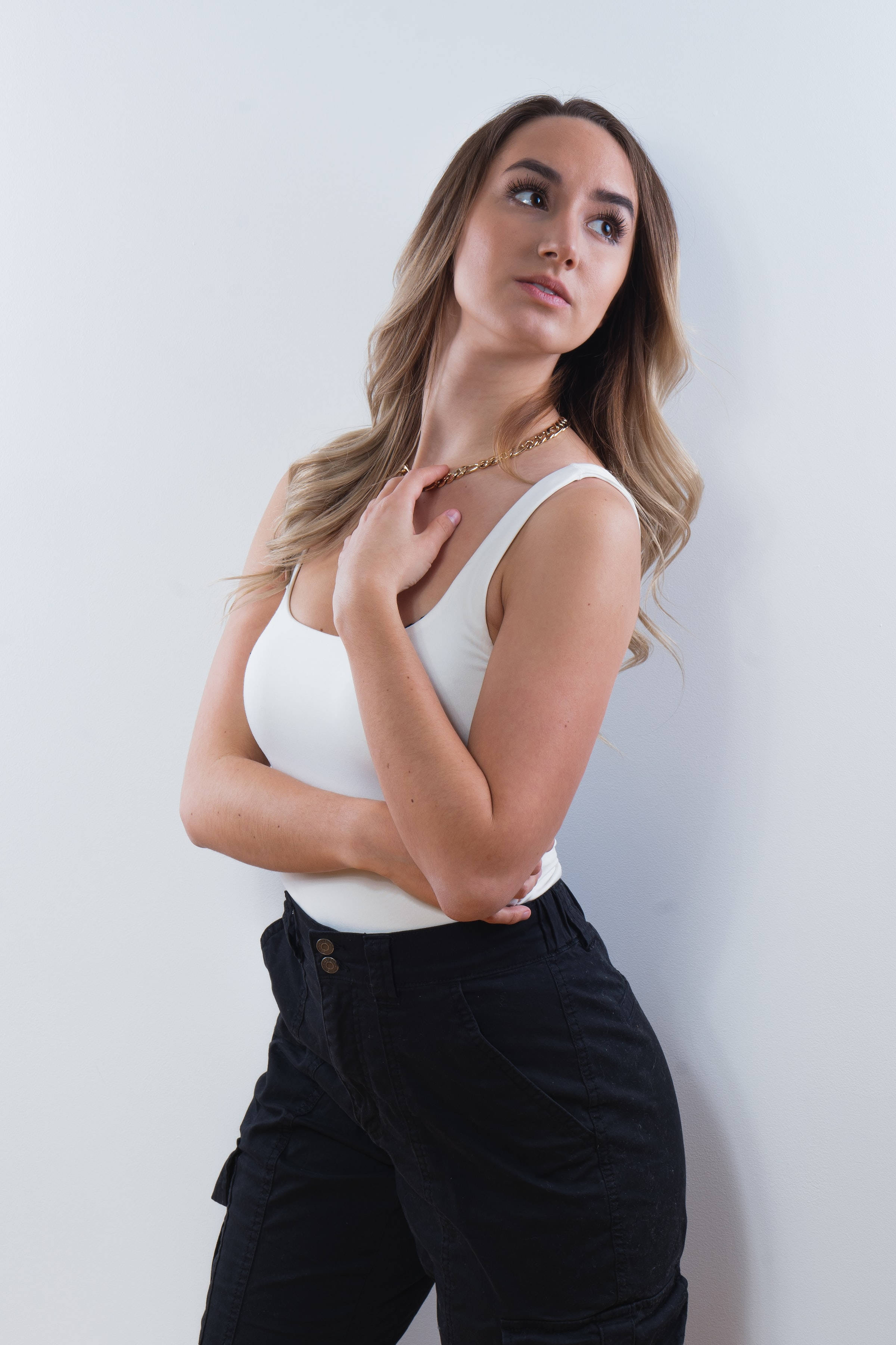 female 桌布 壁紙 — 一位擁有波浪金髮的女性穿著白色背心和黑色褲子，在純白牆前擺姿勢。