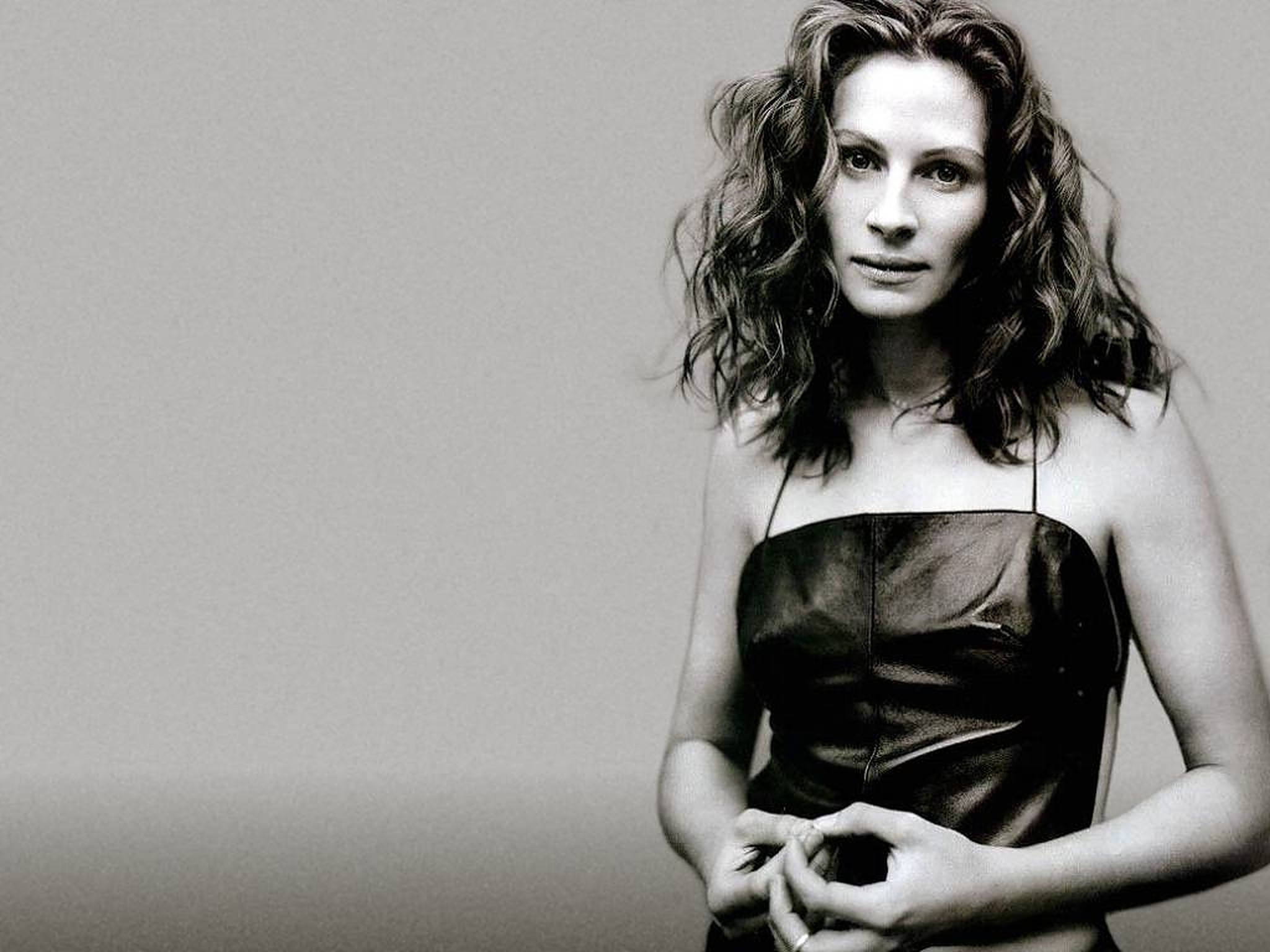 Julia Roberts 桌布 壁紙 — 一位擁有波浪長髮、身穿無肩帶連衣裙的女性，在純灰色背景前直視鏡頭。