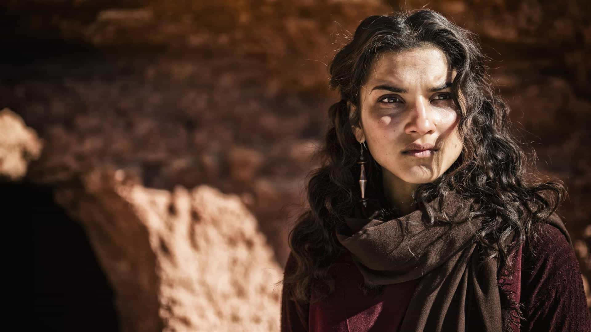 Mary Magdalene 桌布 壁紙 — 一位擁有深色捲髮和圍巾的女性，在陽光照射的岩石洞穴背景下專注地凝視。