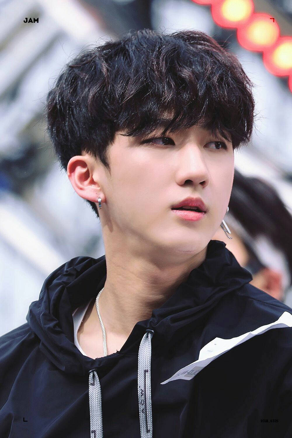 Changbin 桌布 壁紙 — 一位擁有深色捲髮和銀色耳環的年輕男子，穿著帶有白色點綴的黑色連帽衫，若有所思地凝視著。