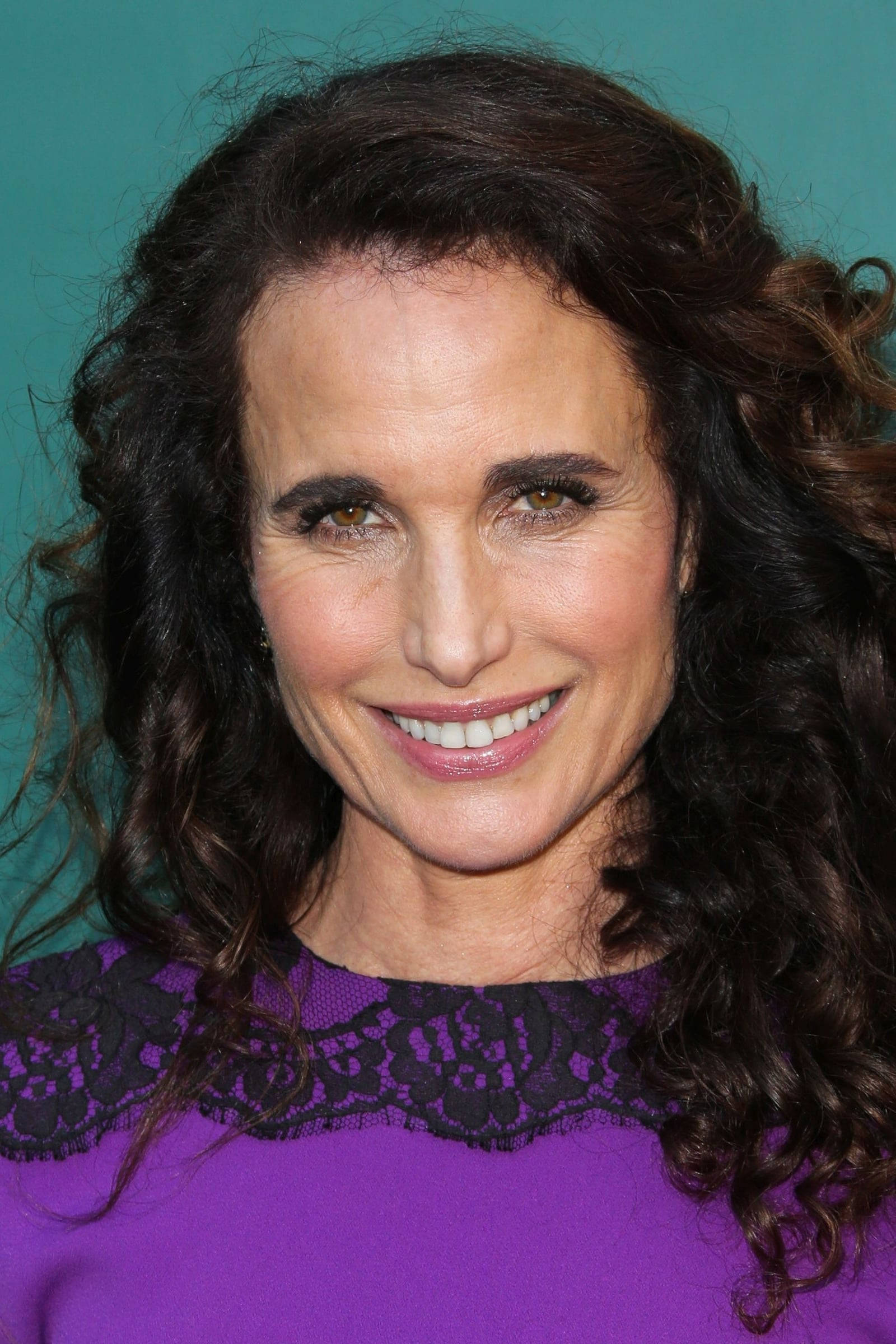 andie macdowell 桌布 壁紙 — 一位擁有深色捲髮的女性在青綠色背景前溫暖微笑的特寫肖像。