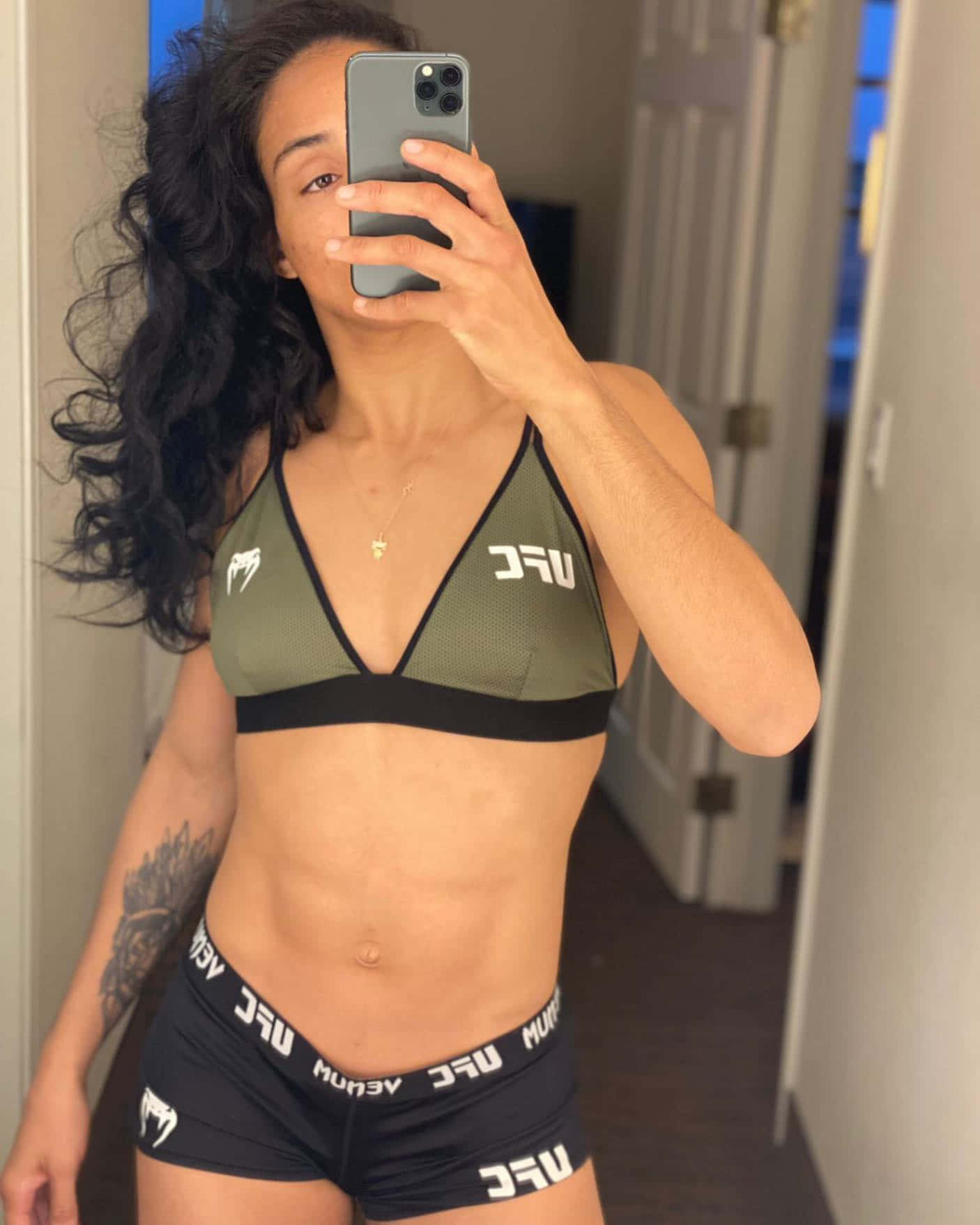 Fitness 桌布 壁紙 — 一位擁有深色捲髮的女性穿著UFC運動胸罩和短褲，在鏡子前自拍，展示她結實的身材。