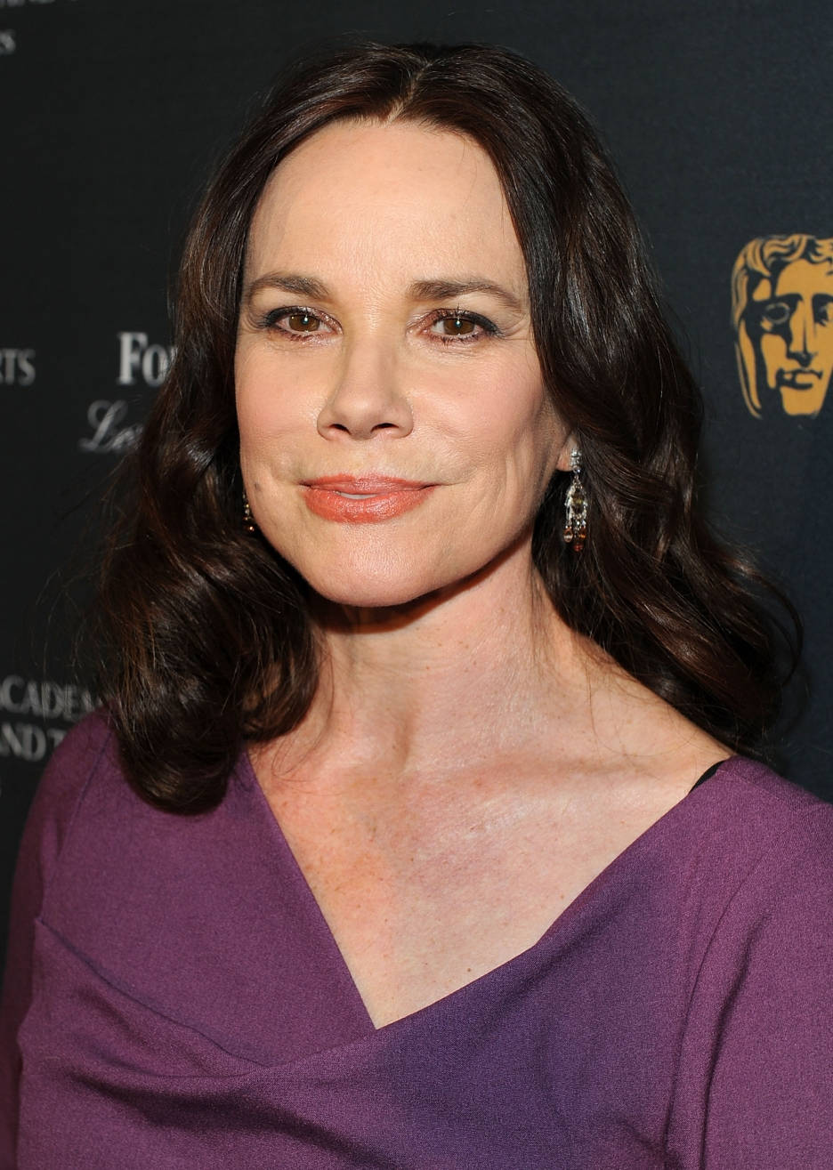Celebrity 桌布 壁紙 — 一位擁有深色波浪長髮、身穿紫色連衣裙的女性，在帶有BAFTA標誌的黑色背景前對著鏡頭溫柔微笑。