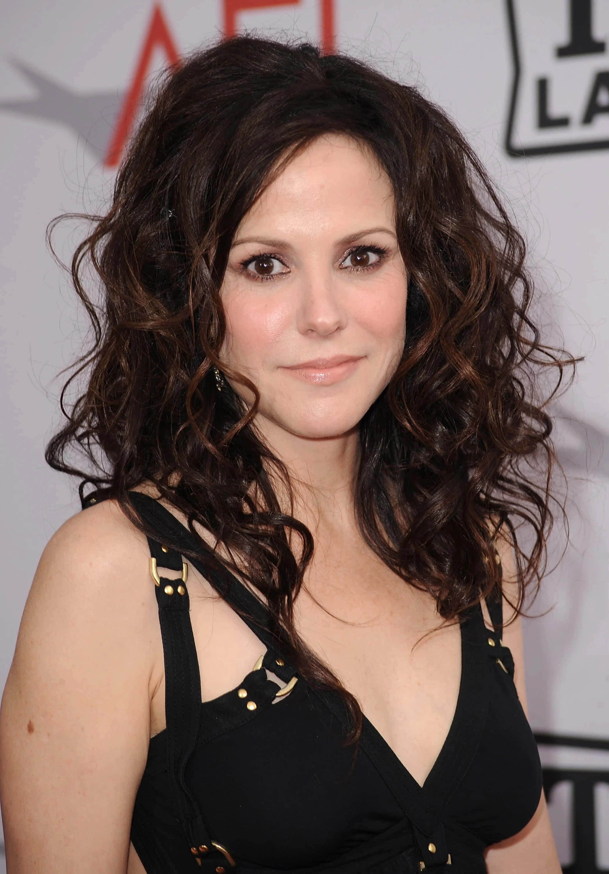 mary louise parker 桌布 壁紙 — 一位擁有深色波浪長髮、身穿黑色上衣的女性在活動中對著鏡頭溫柔微笑。