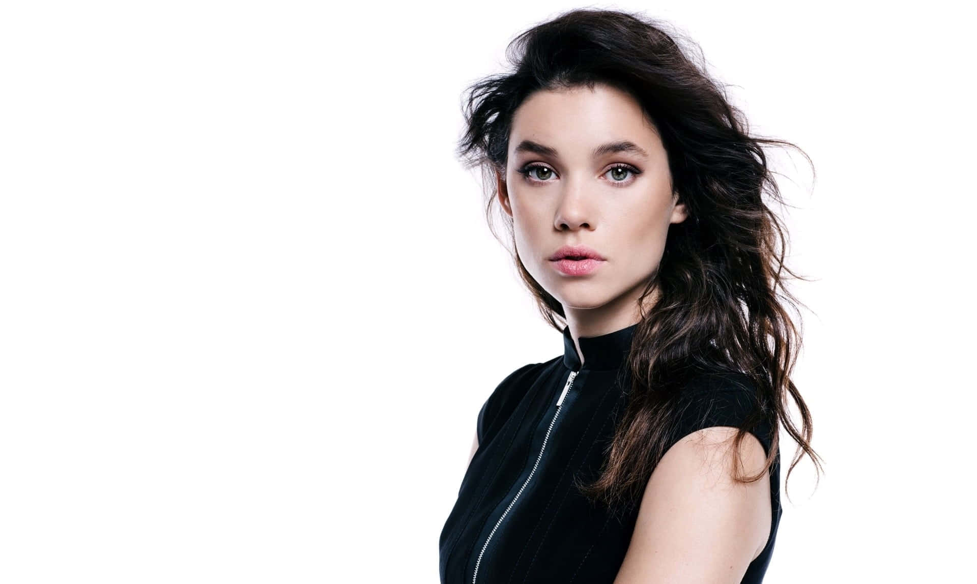 Astrid Berges Frisbey 桌布 壁紙 — 一位擁有深色波浪長髮和銳利眼神的女性，穿著黑色拉鍊上衣，背景是純白色。