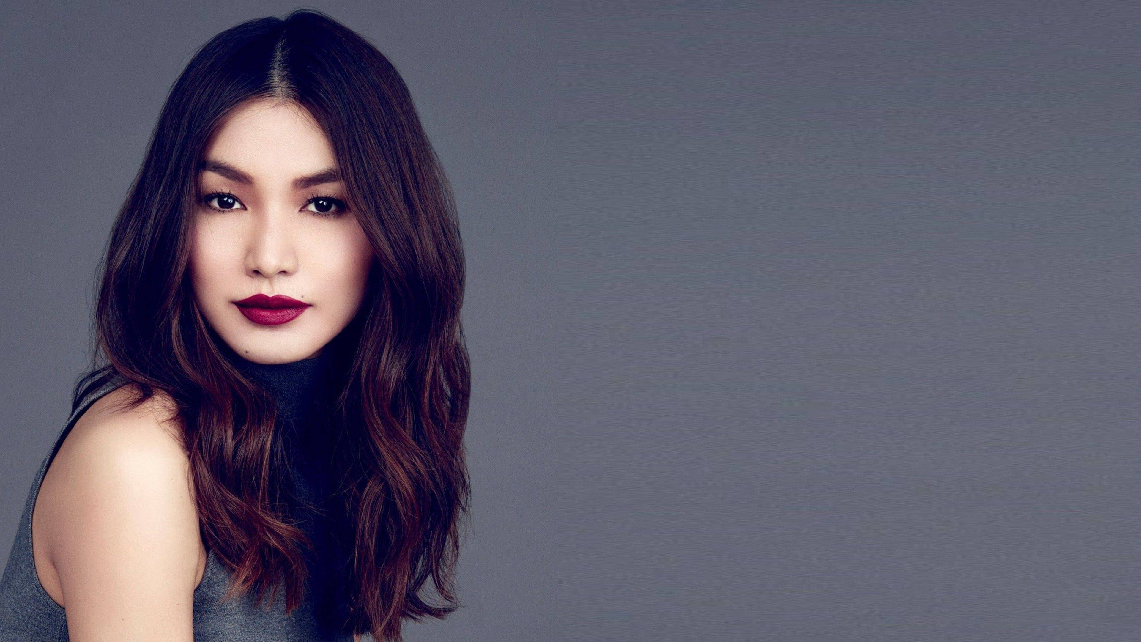 Gemma Chan 桌布 壁紙 — 一位擁有深色波浪長髮和鮮豔紅唇的女性，在柔和的灰色攝影棚背景前直視鏡頭。