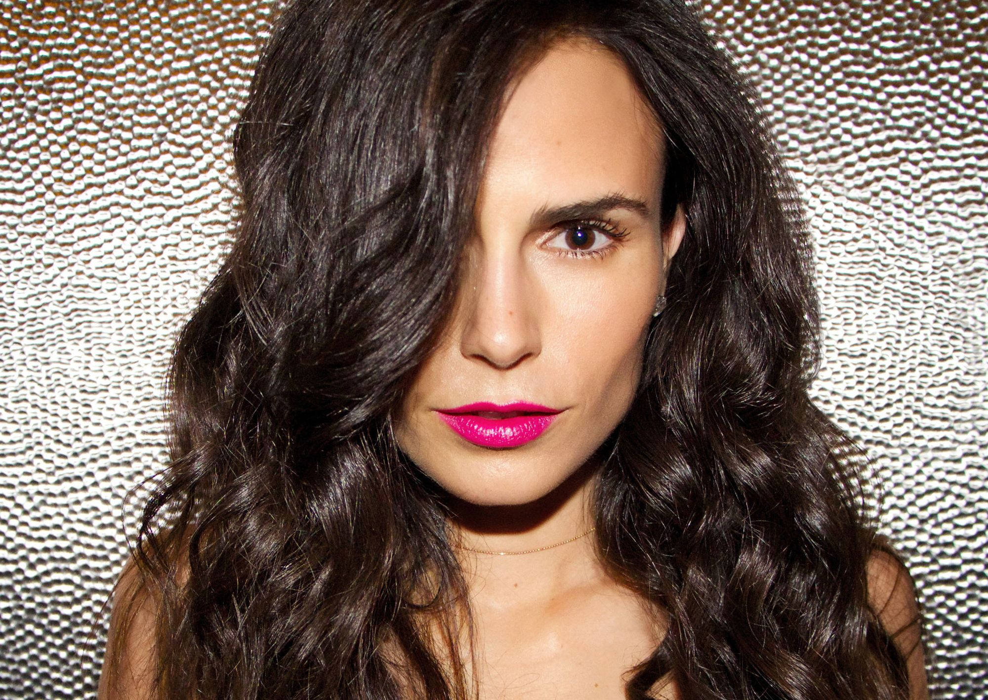 Jordana Brewster 桌布 壁紙 — 一位擁有深色波浪頭髮和大膽粉紅嘴唇的女性，在帶有紋理的銀色背景下強烈凝視。