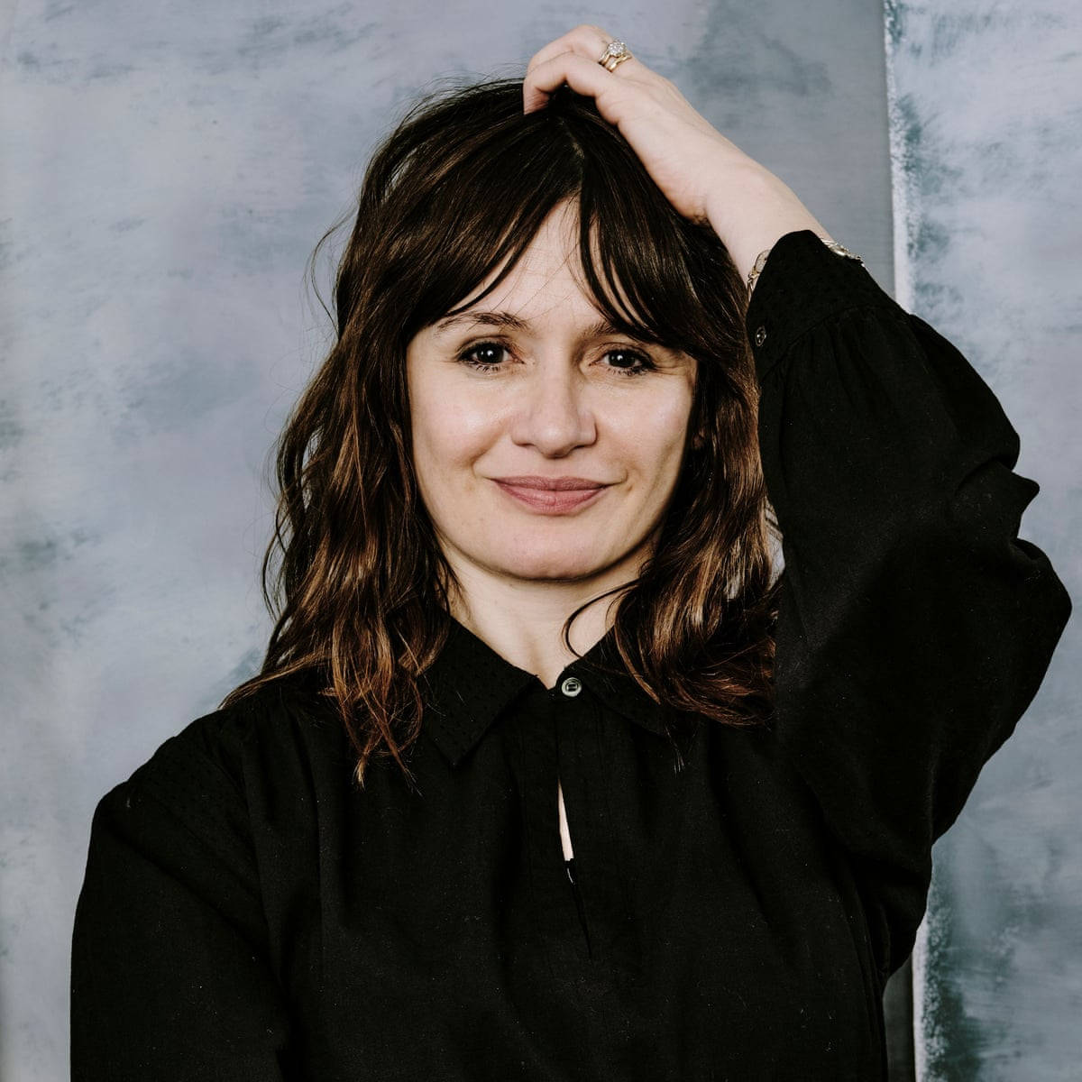 Celebrity 桌布 壁紙 — 一位擁有深色波浪頭髮和溫柔微笑的女性，在紋理灰色背景前將手舉到頭部。