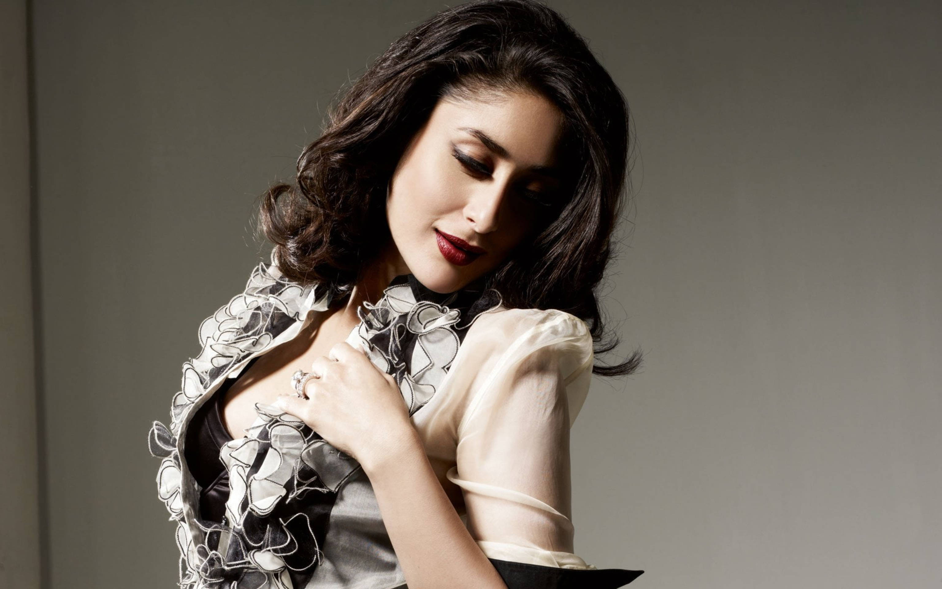 Kareena 桌布 壁紙 — 一位擁有深色波浪頭髮和紅唇的女性，在純灰色背景下低頭凝視，同時觸摸她的花卉圖案襯衫。