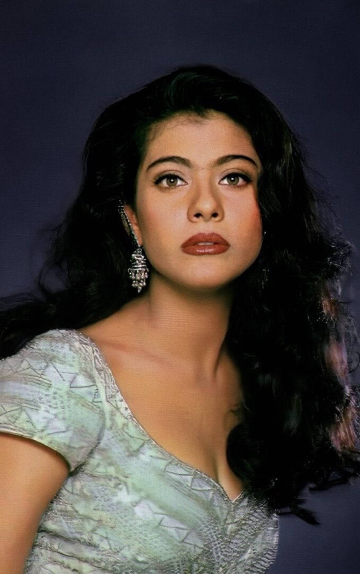Kajol 桌布 壁紙 — 一位擁有深色波浪頭髮和華麗耳環的女性，穿著淺綠色圖案上衣，在深紫色背景下向前凝視。