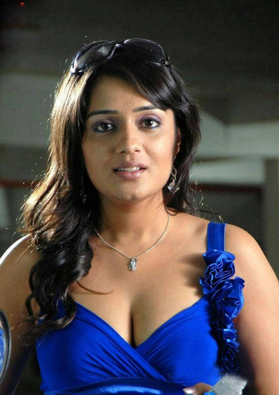 telugu 桌布 壁紙 — 一位擁有深色波浪髮、頭頂架著太陽眼鏡的女性，穿著鮮豔的藍色荷葉邊連衣裙，對著鏡頭溫柔微笑。
