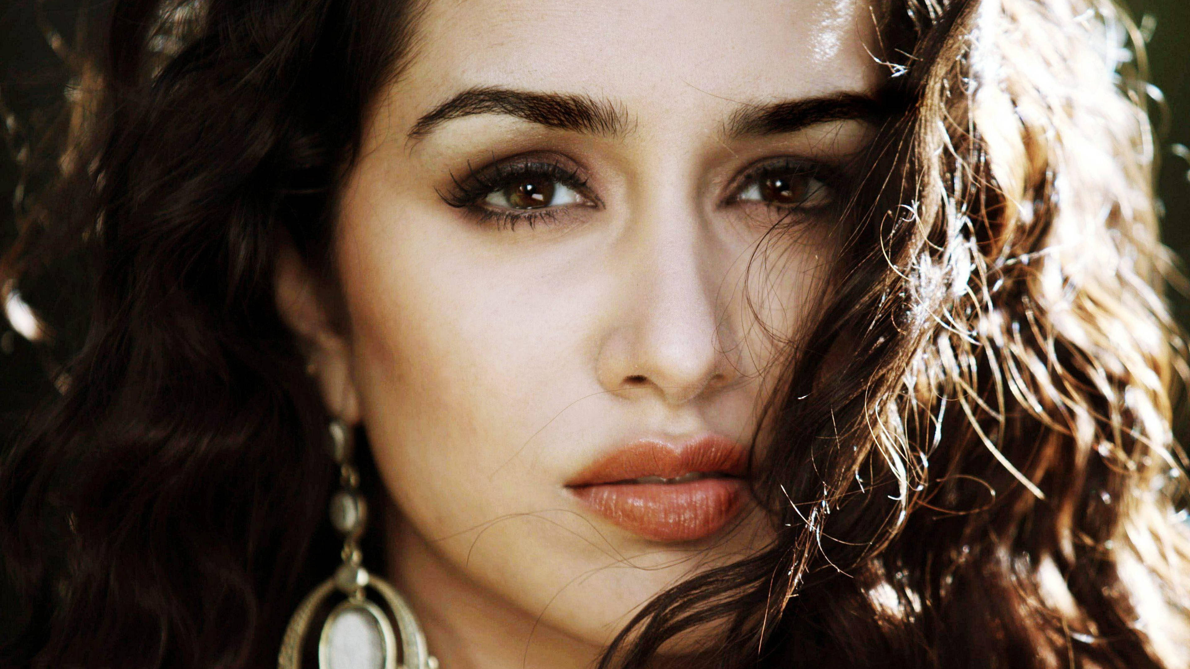 Shraddha Kapoor 桌布 壁紙 — 一位擁有深色波浪髮和金色耳環的女性特寫肖像，沐浴在溫暖的陽光下。