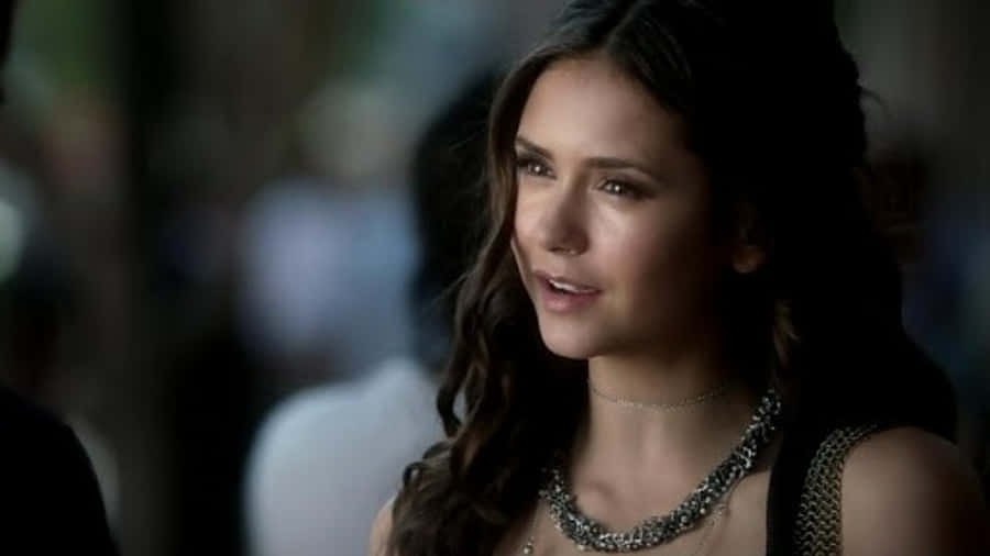 Vampire Diaries 桌布 壁紙 — 一位擁有深色波浪髮和銀色項鍊的女性在昏暗的燈光下沉思地凝視。