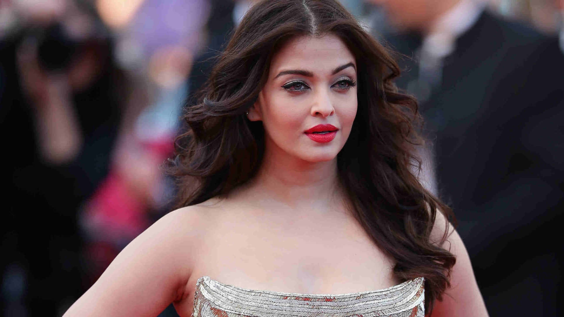 Aishwarya Rai 桌布 壁紙 — 一位擁有深色波浪髮和鮮豔紅唇的女性在紅地毯活動中穿著閃亮的無肩帶禮服。