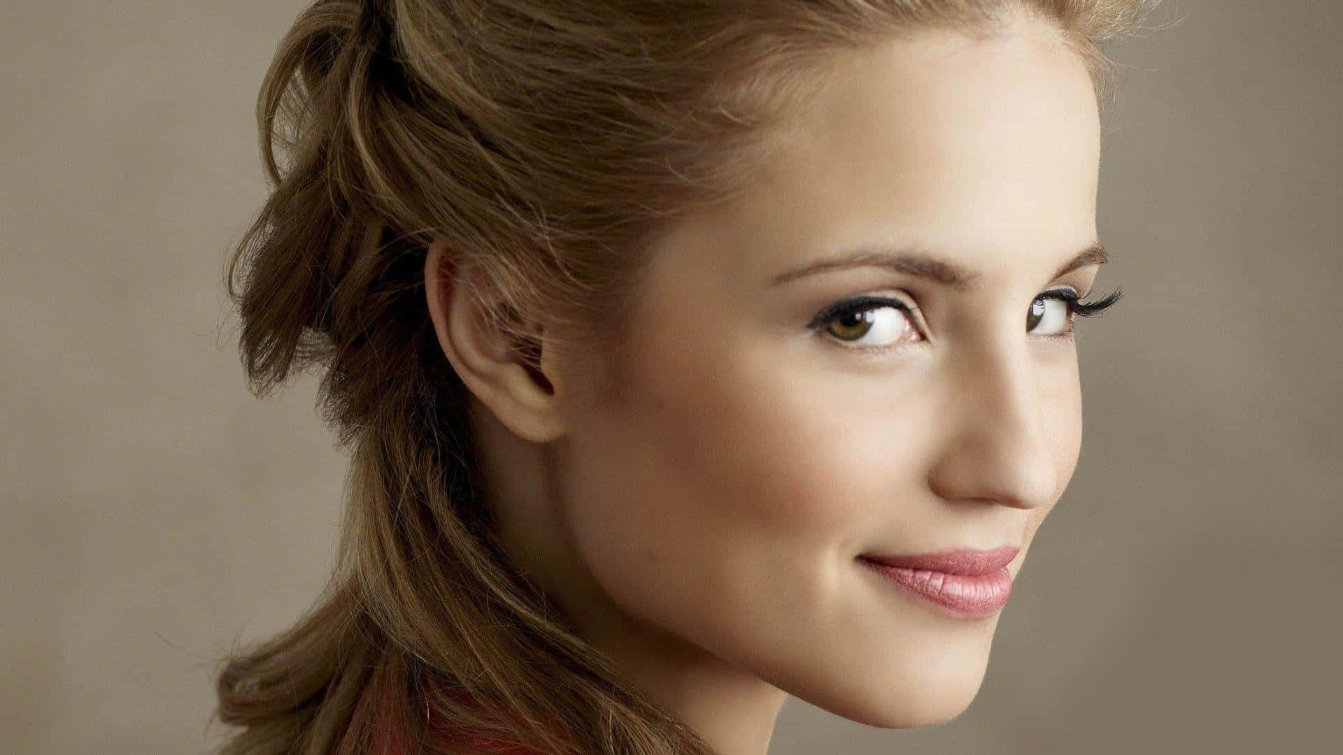 dianna agron 桌布 壁紙 — 一位擁有溫暖棕色頭髮、半紮起髮型的女性，在中性米色背景前溫柔微笑的特寫肖像。