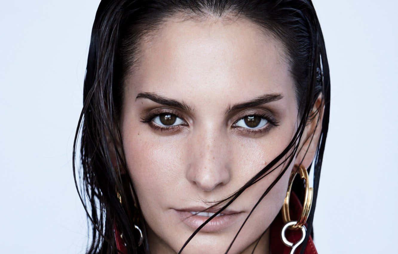 Genesis Rodriguez 桌布 壁紙 — 一位擁有濕黑髮和大膽金色圓環耳環的女子的特寫肖像，背景為純色淺色。