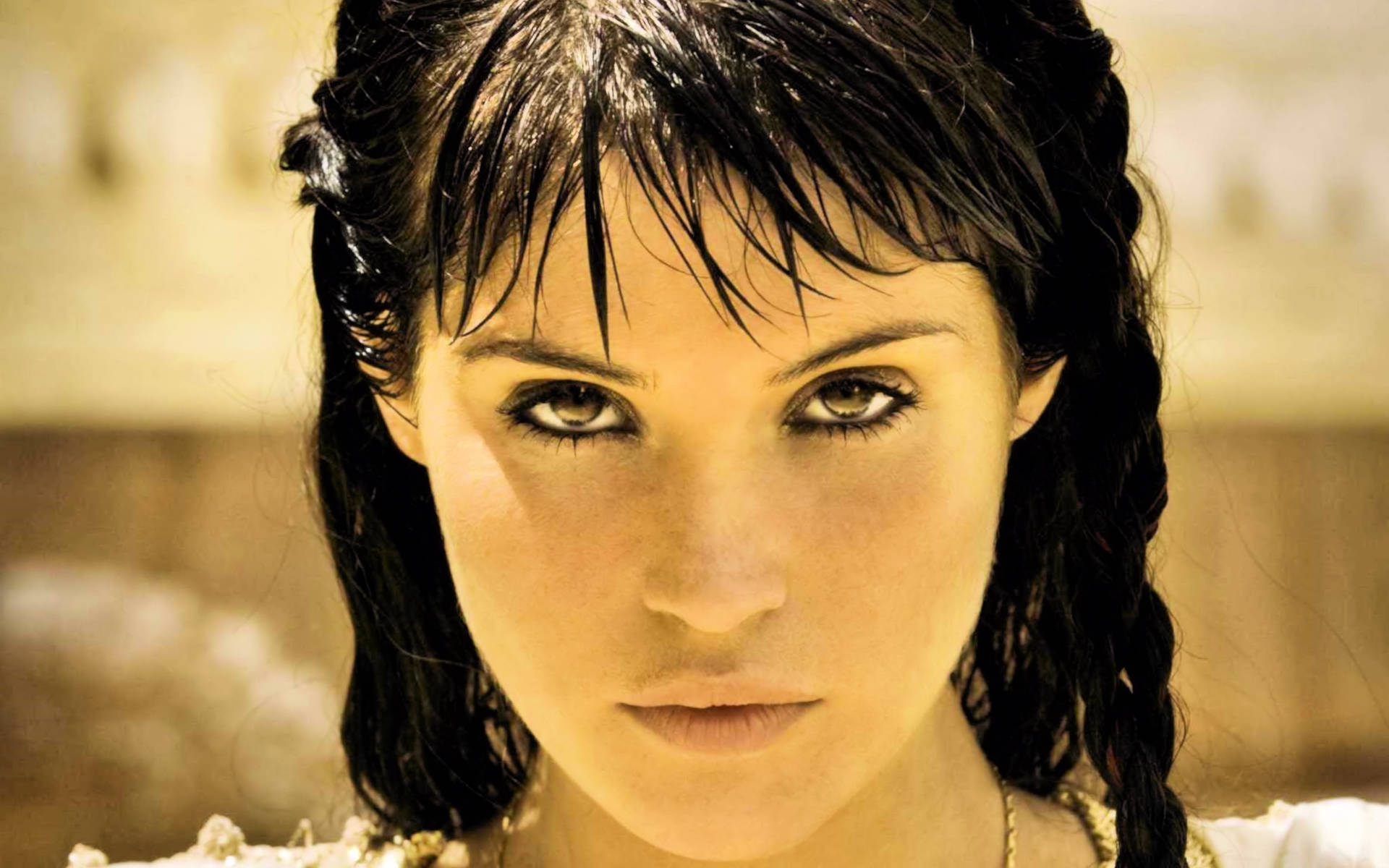 Gemma Arterton 桌布 壁紙 — 一位擁有濕黑髮和強烈眼神的女性特寫肖像，在溫暖的金色燈光下。