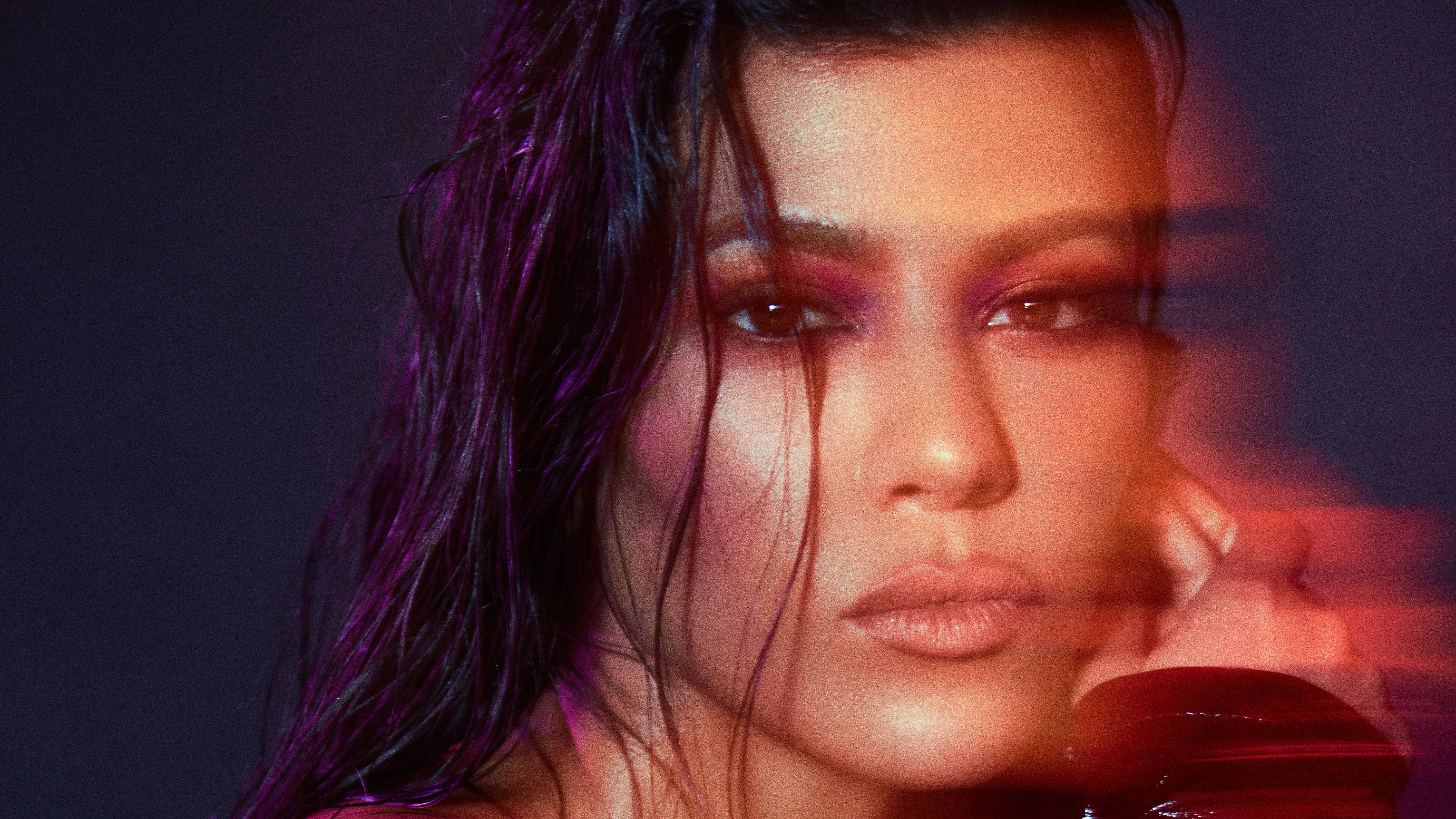 Kourtney 桌布 壁紙 — 一位擁有濕黑髮和煙熏妝容的女性在戲劇性的紫色和紅色燈光下強烈凝視。