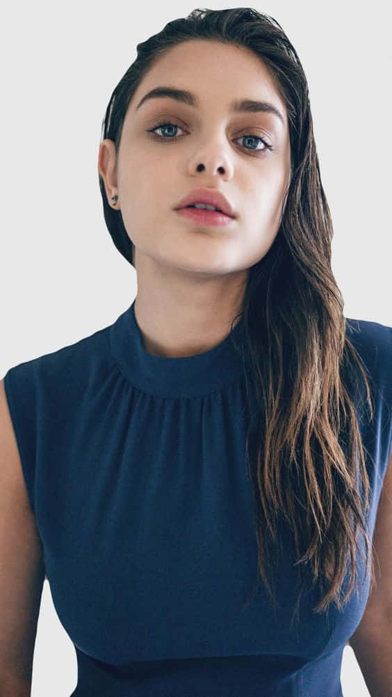 Odeya Rush 桌布 壁紙 — 一位擁有濕黑髮和藍眼睛的女性，穿著海軍藍無袖上衣，在純色背景下直視鏡頭。